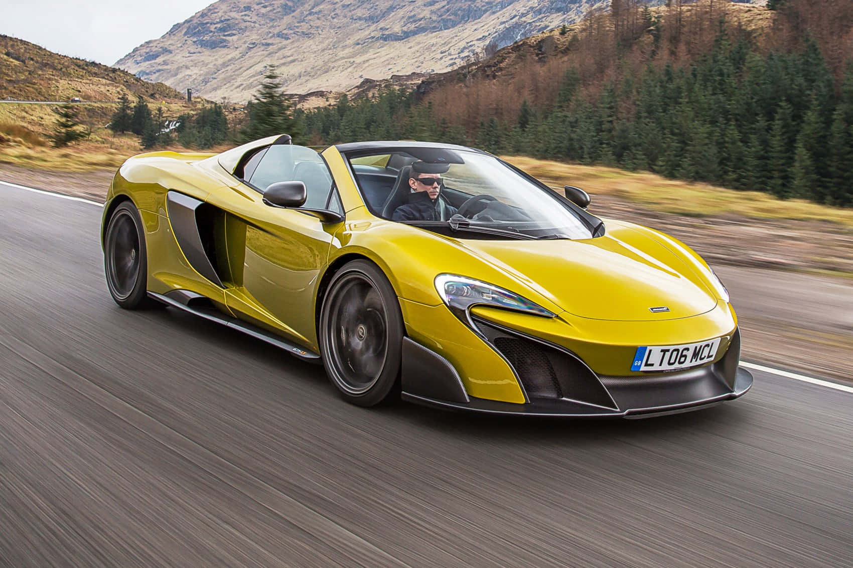 Mclaren 675lt Spider 桌布 壁紙 — 一輛充滿活力的黃色McLaren跑車，在蜿蜒的山路上疾馳，司機戴著太陽眼鏡。