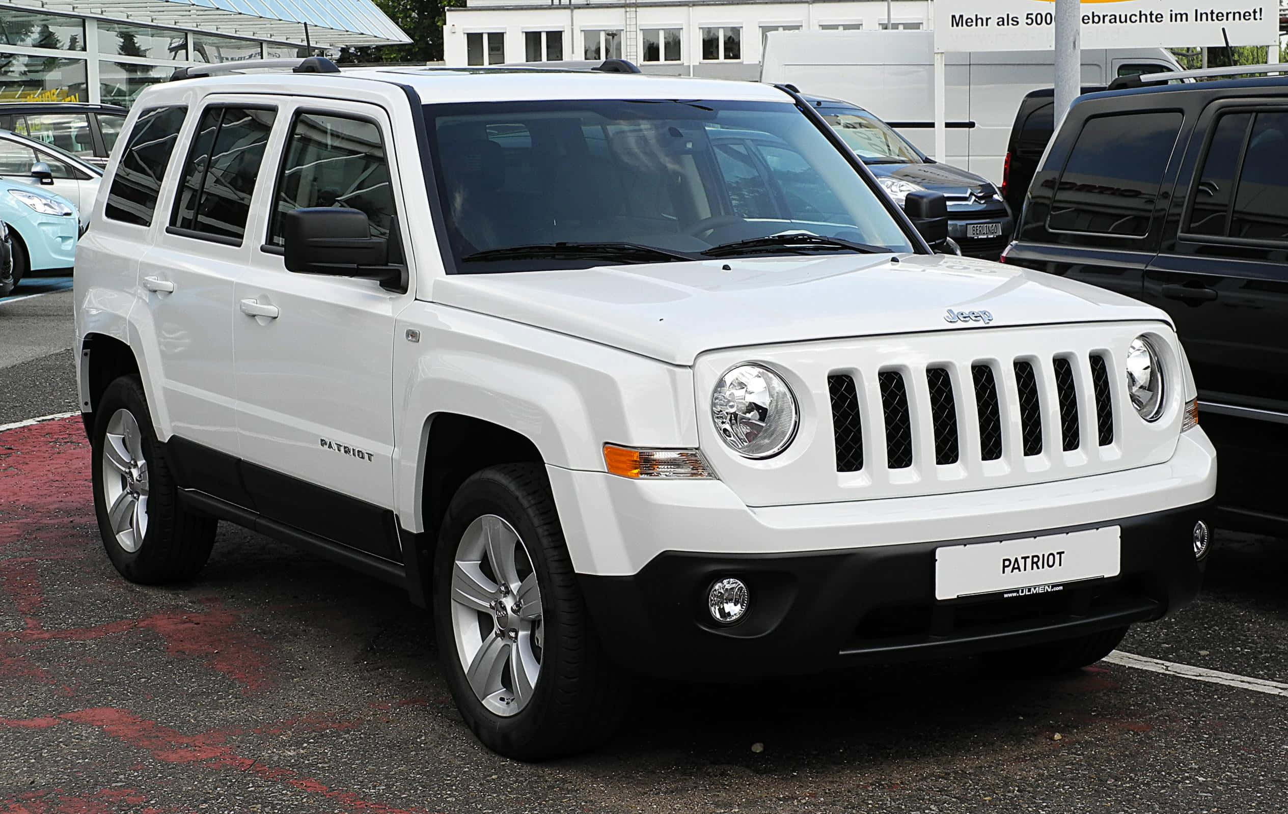 Jeep Patriot 桌布 壁紙 — 一輛純白色的Jeep Patriot SUV在明亮的日光下停放在一個停車場，旁邊有其他車輛。