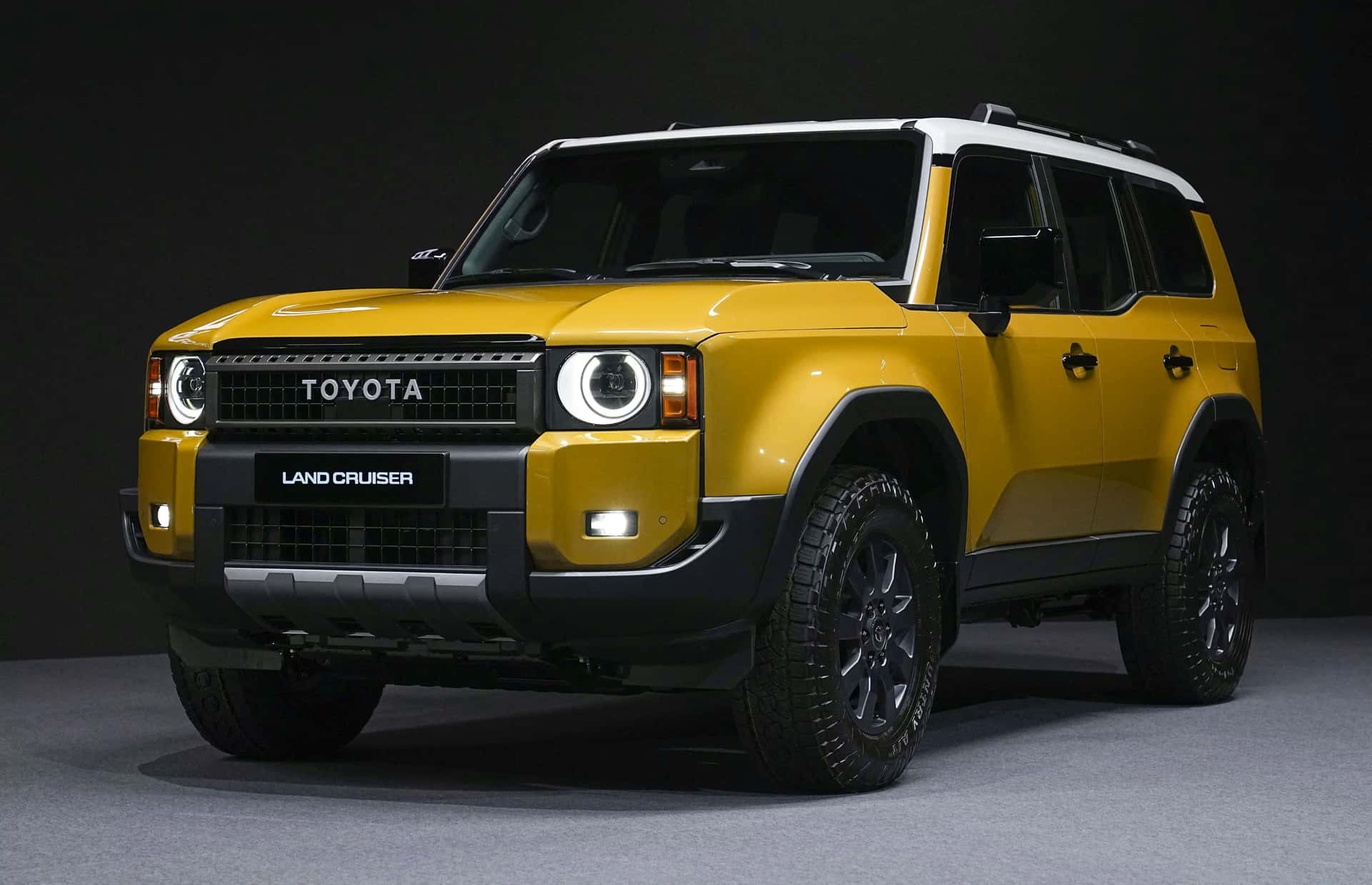  壁紙 — 一輛大膽的黃色豐田 Land Cruiser SUV，帶有黑色飾件和堅固輪胎，在深色工作室背景下擺拍。
