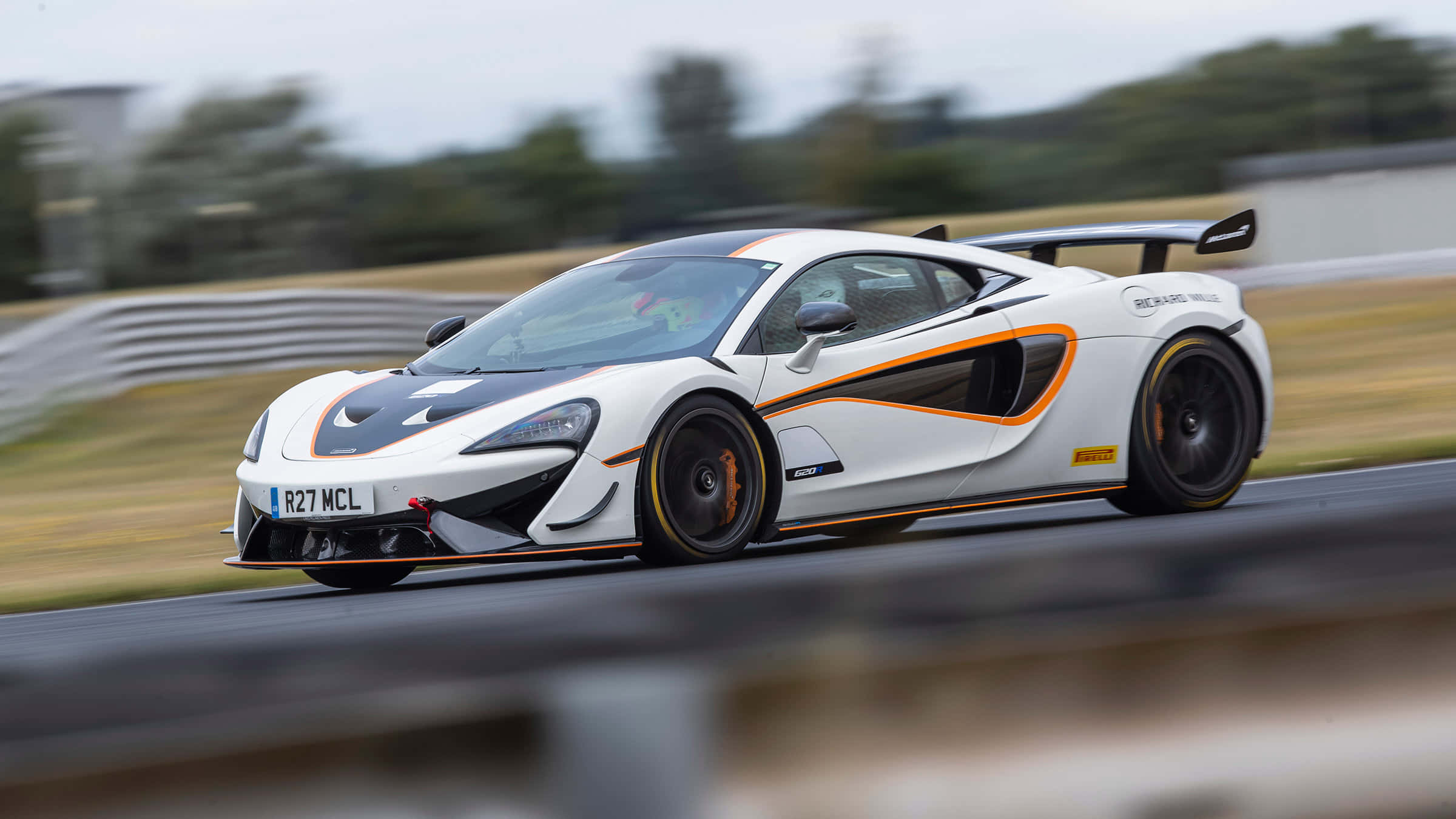 Mclaren 620r 桌布 壁紙 — 一輛帶有橙色點綴的白色McLaren跑車在賽道上疾馳，背景是模糊的綠色植物。