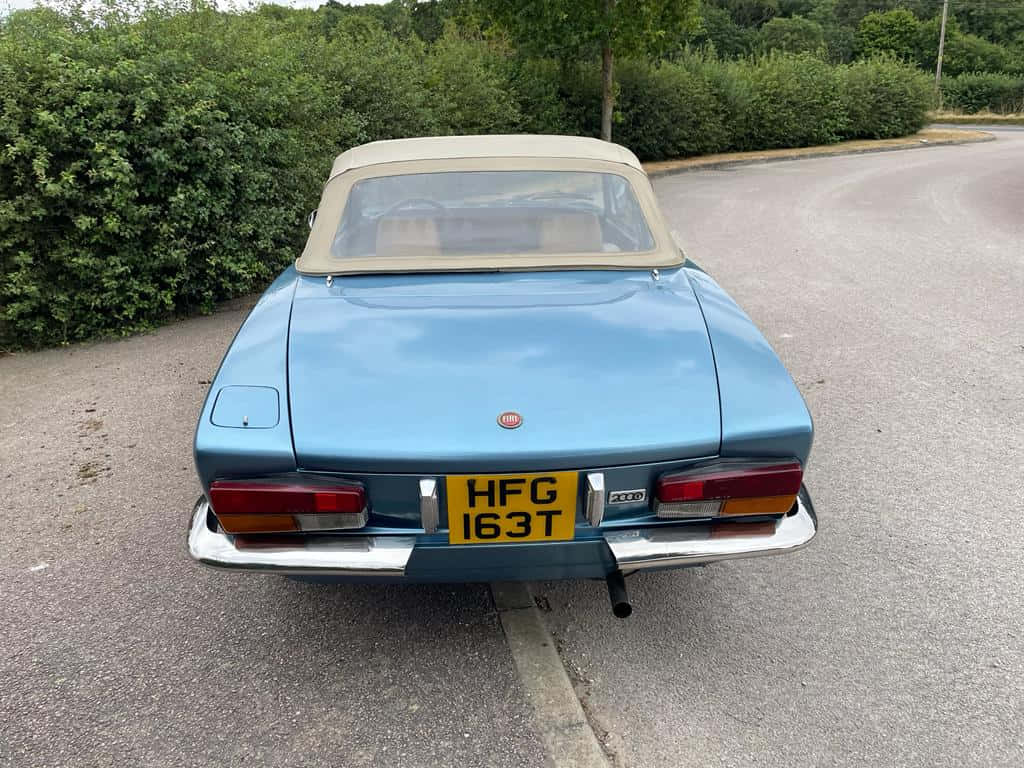 Fiat 124 Spider 桌布 壁紙 — 一輛復古淺藍色Fiat 124 Spider開篷車停在瀝青路上，背景有綠色樹籬。