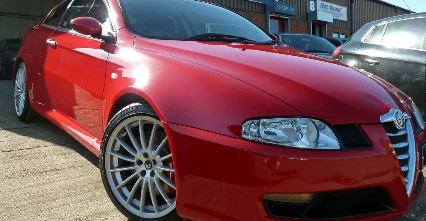 Alfa Romeo Gt 桌布 壁紙 — 一輛光澤的紅色愛快羅密歐雙門跑車停放在戶外，陽光反射在其拋光的引擎蓋和合金輪圈上。