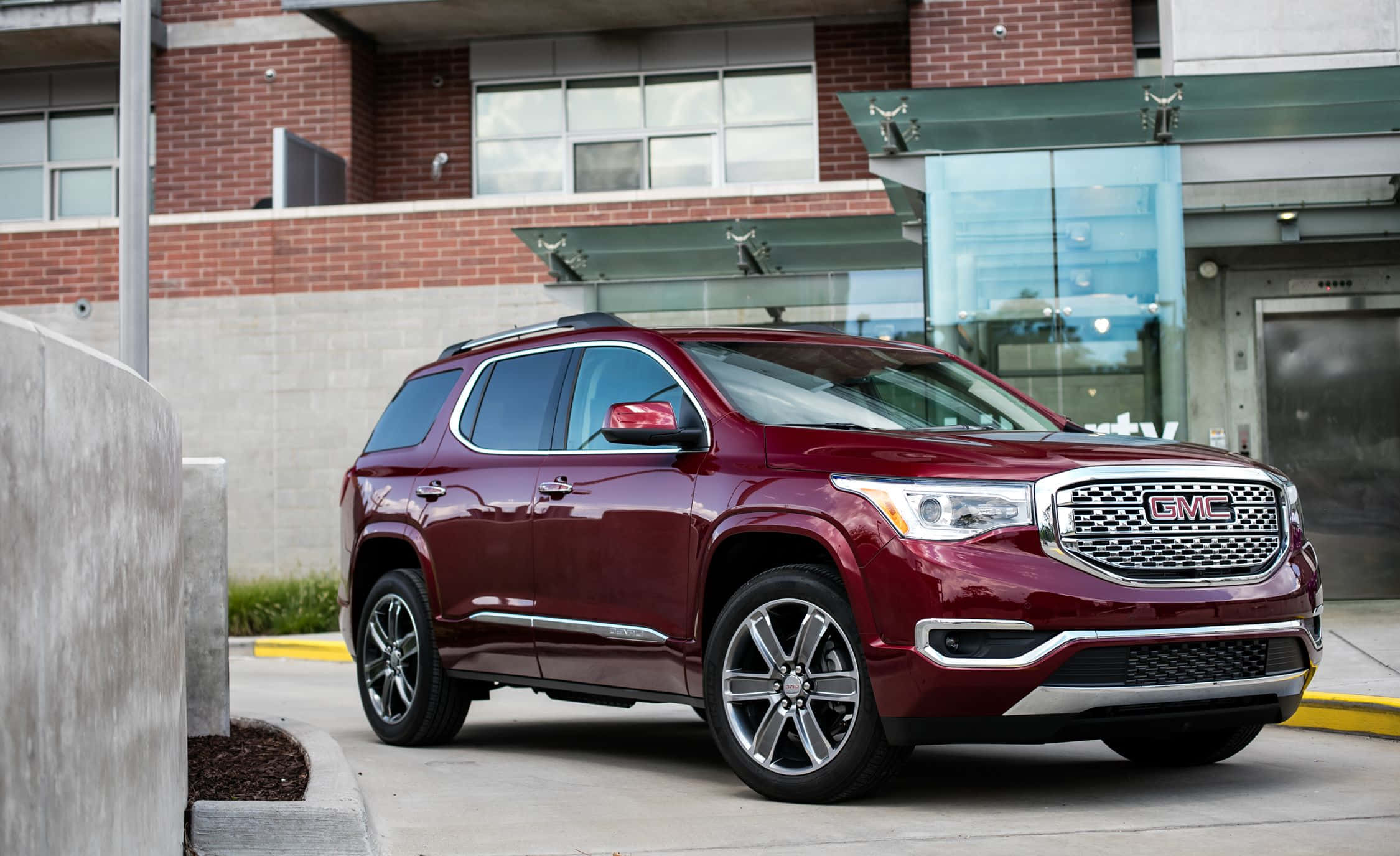 Gmc Acadia 桌布 壁紙 — 一輛光澤的棗紅色GMC Acadia SUV停泊在現代磚和玻璃建築入口處。
