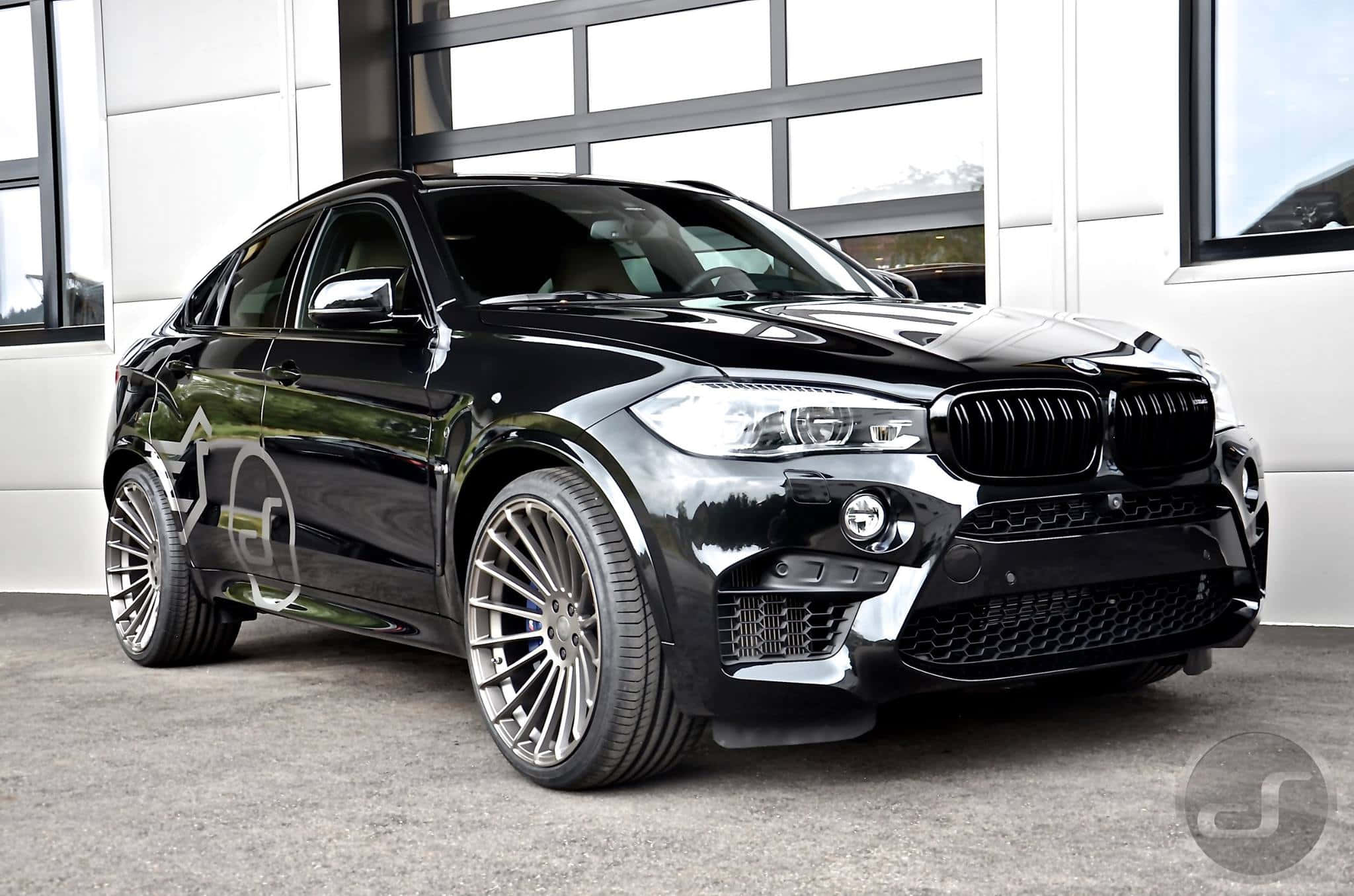Bmw X6 桌布 壁紙 — 一輛光澤黑色BMW X6 M配備定制銀色輪圈，停放在現代白色車庫內。