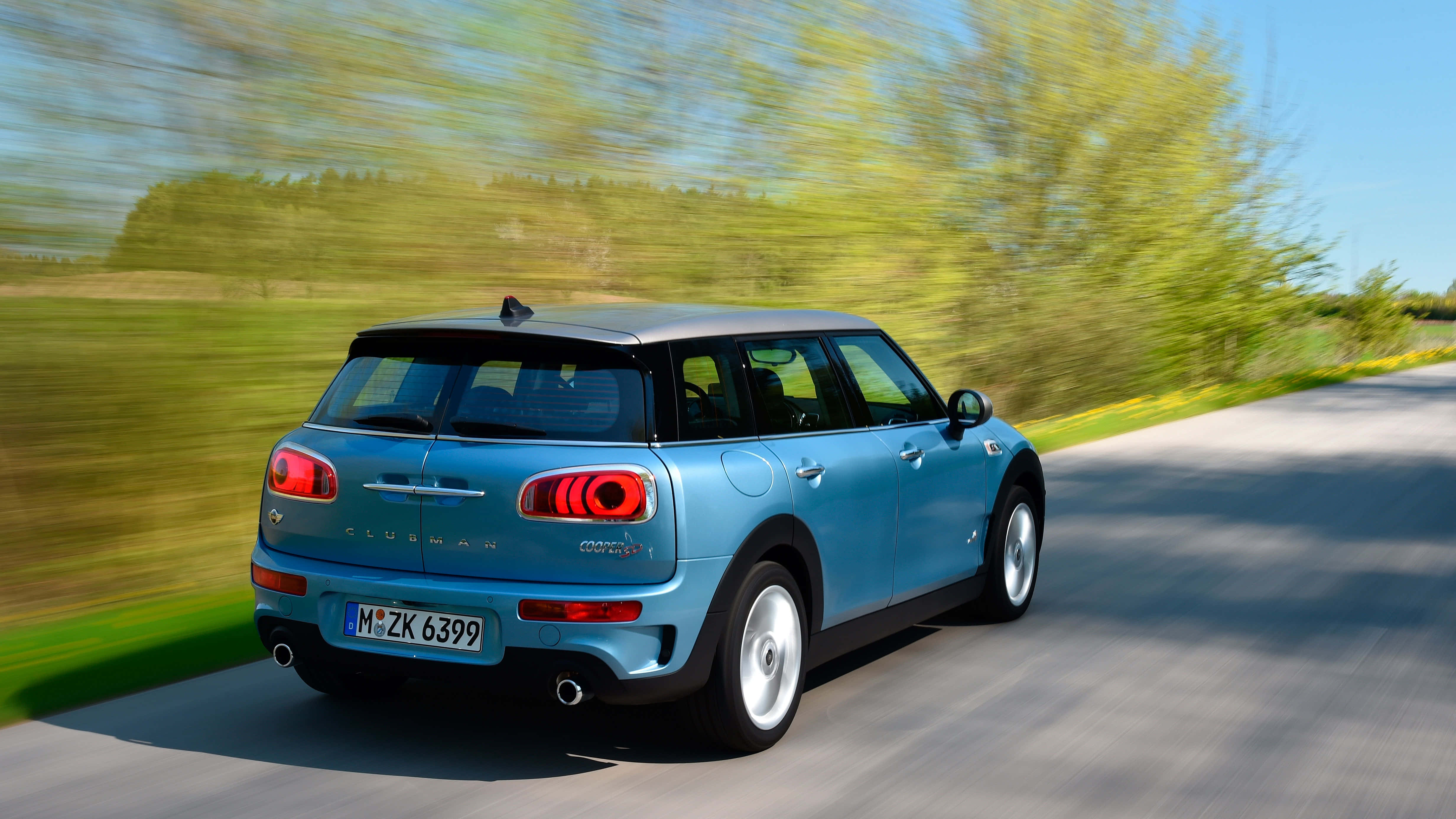 Mini Cooper S Clubman All4 桌布 壁紙 — 一輛藍色MINI Clubman在陽光明媚的鄉村道路上疾馳，周圍的綠色樹木和草地因運動而模糊。