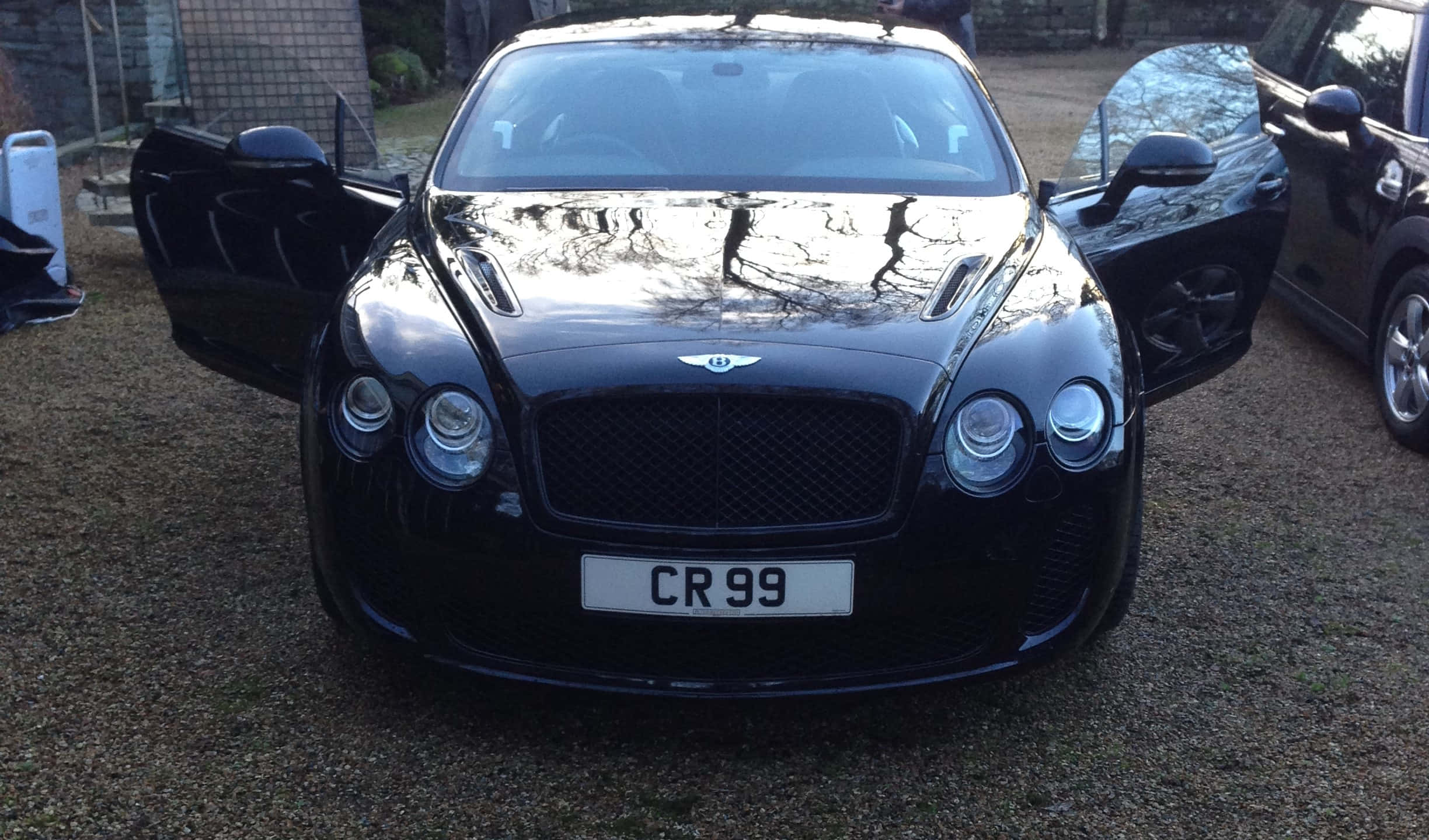 Bentley Continental Supersports 桌布 壁紙 — 一輛亮黑色賓利 Continental GT 打開車門停在後院的碎石地上。