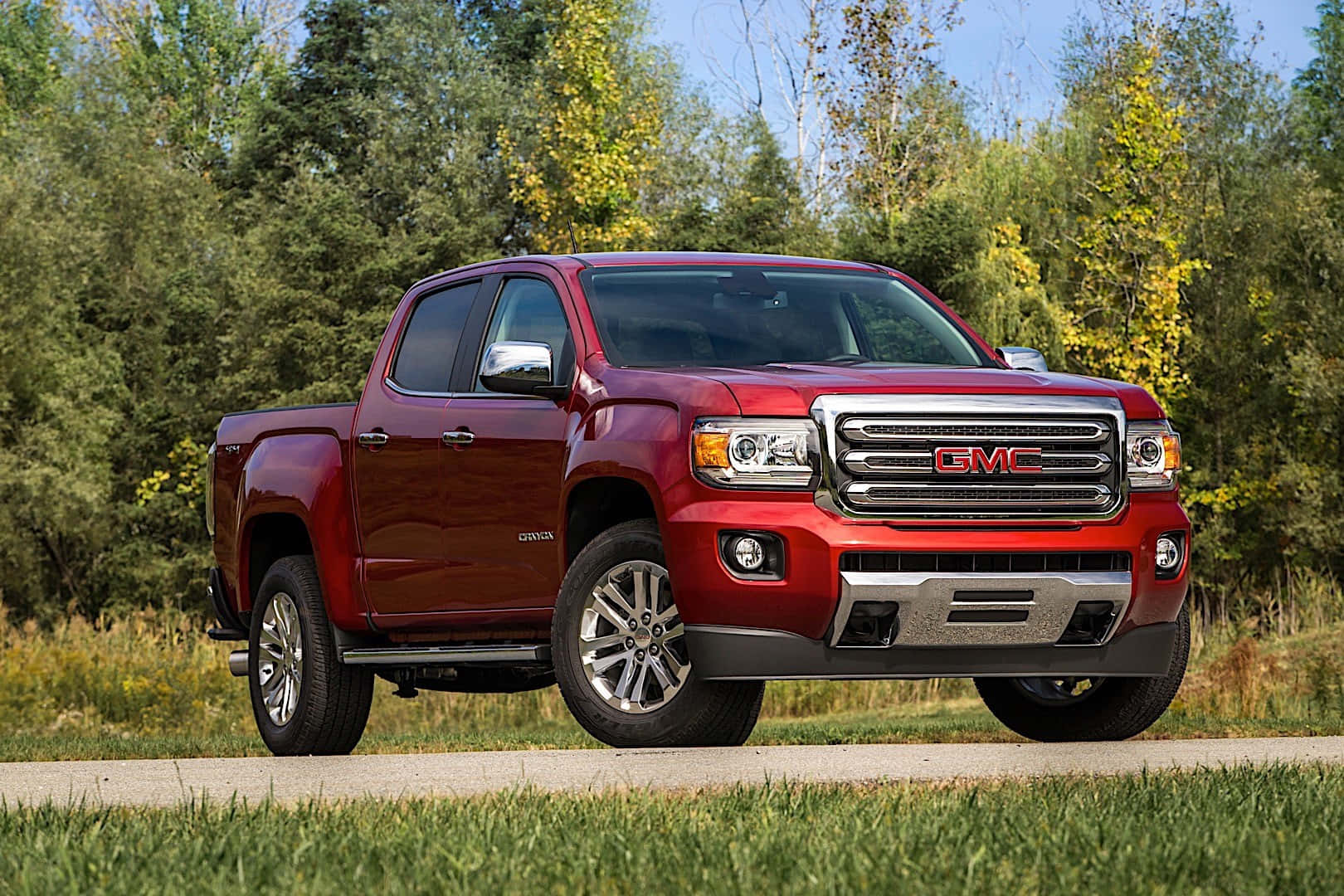 Gmc Canyon 桌布 壁紙 — 一輛亮紅色的GMC Canyon皮卡車停在鋪砌的道路上，周圍是秋天的樹木和綠草，頭頂是清澈的藍天。