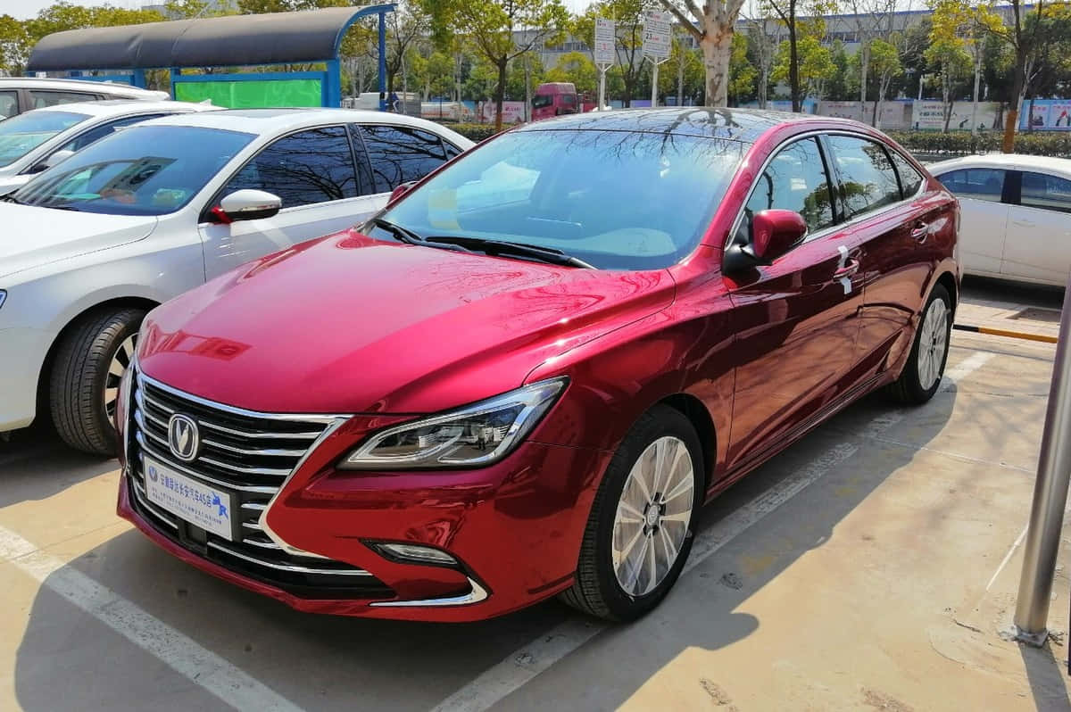  壁紙 — 一輛亮紅色轎車停放在陽光明媚的戶外停車場，背景有其他汽車和樹木。
