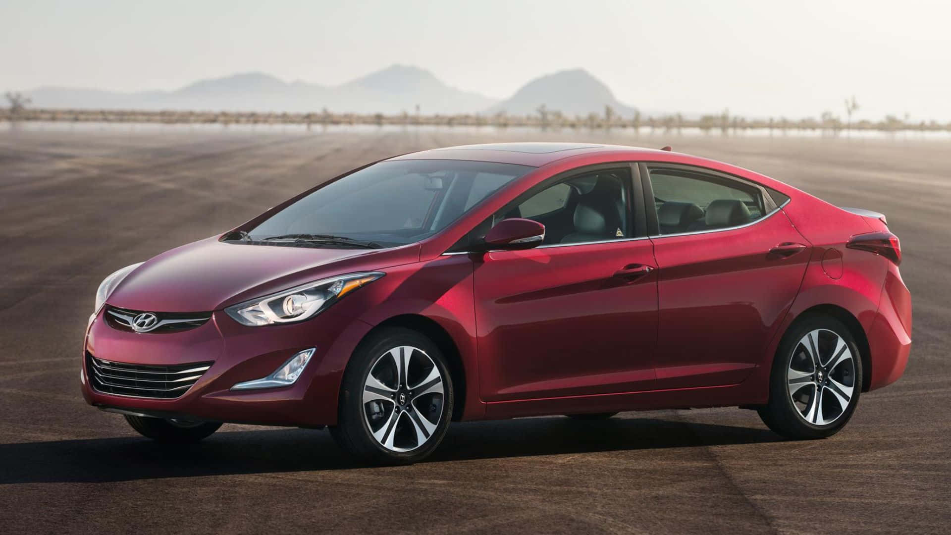 Hyundai Elantra 桌布 壁紙 — 一輛亮紅色現代Elantra房車停泊在廣闊的沙漠道路上，遠山在朦朧的天空下。