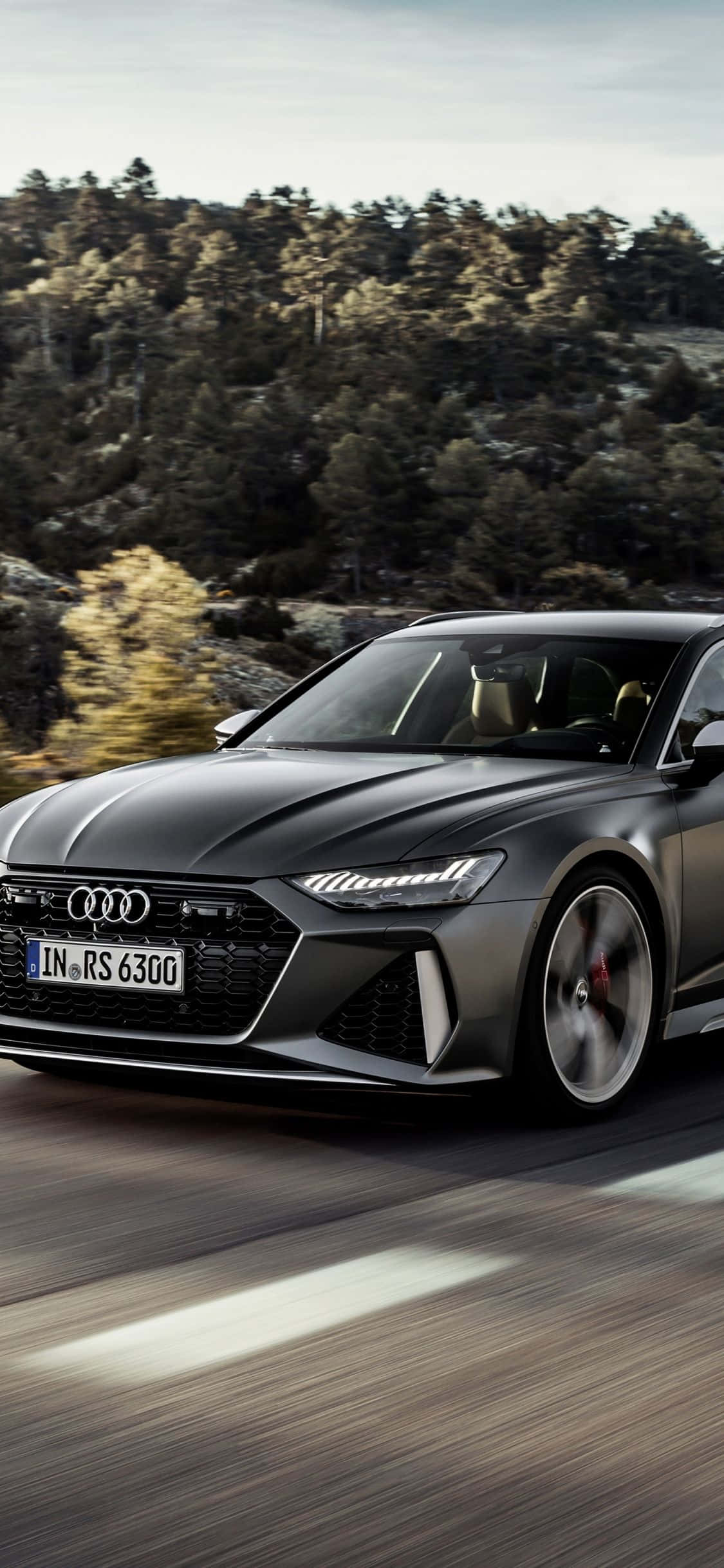 Audi Rs6 桌布 壁紙 — 一輛流線型啞光黑色奧迪RS 6 Avant在茂密森林中蜿蜒的道路上疾馳，帶有動態模糊效果。