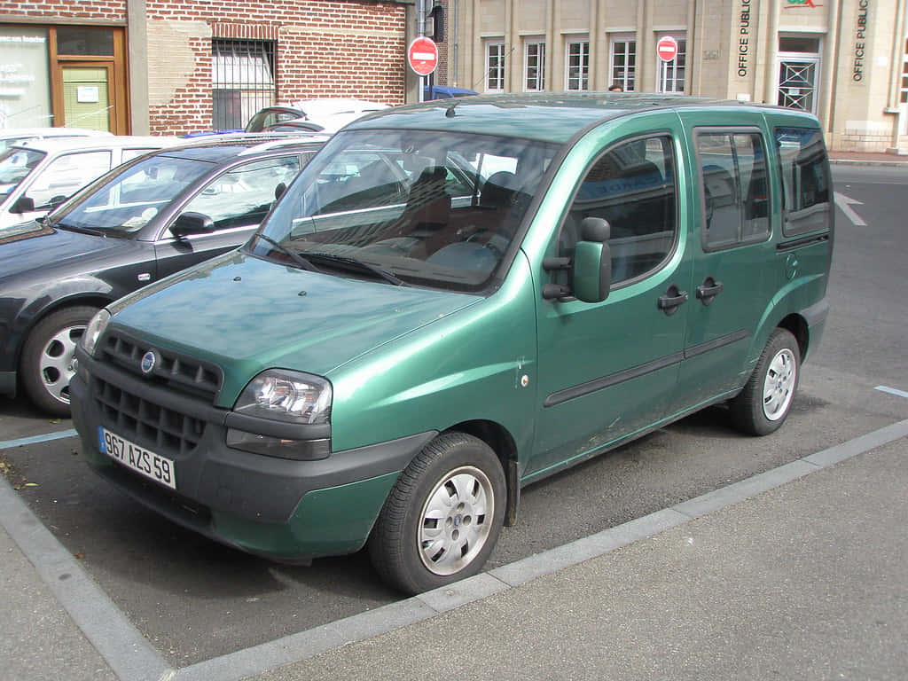  壁紙 — 一輛綠色Fiat Multipla小型貨車停泊在城市地塊，附近有磚砌建築和其他汽車。