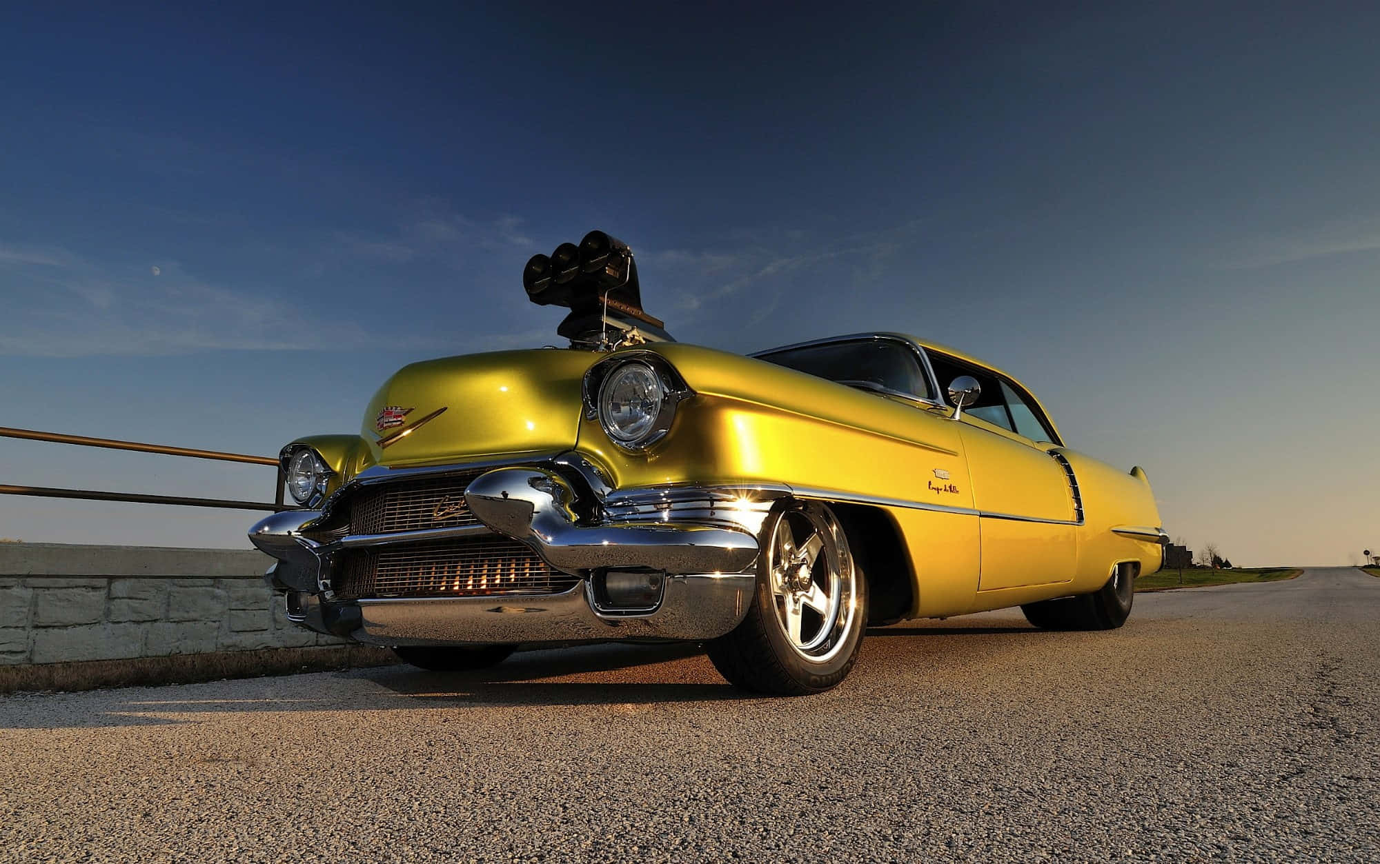 Cadillac Deville 桌布 壁紙 — 一輛閃亮的黃色經典汽車，帶有鍍鉻細節，在日落時分停在路邊，天空清澈湛藍。