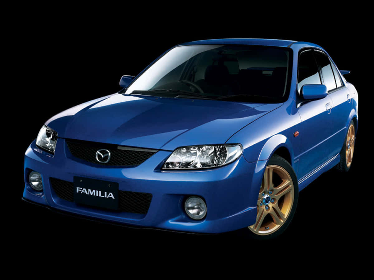 Mazda Protege 桌布 壁紙 — 一輛閃亮的藍色萬事得Familia房車配金色輪圈，在純黑色背景下脫穎而出。