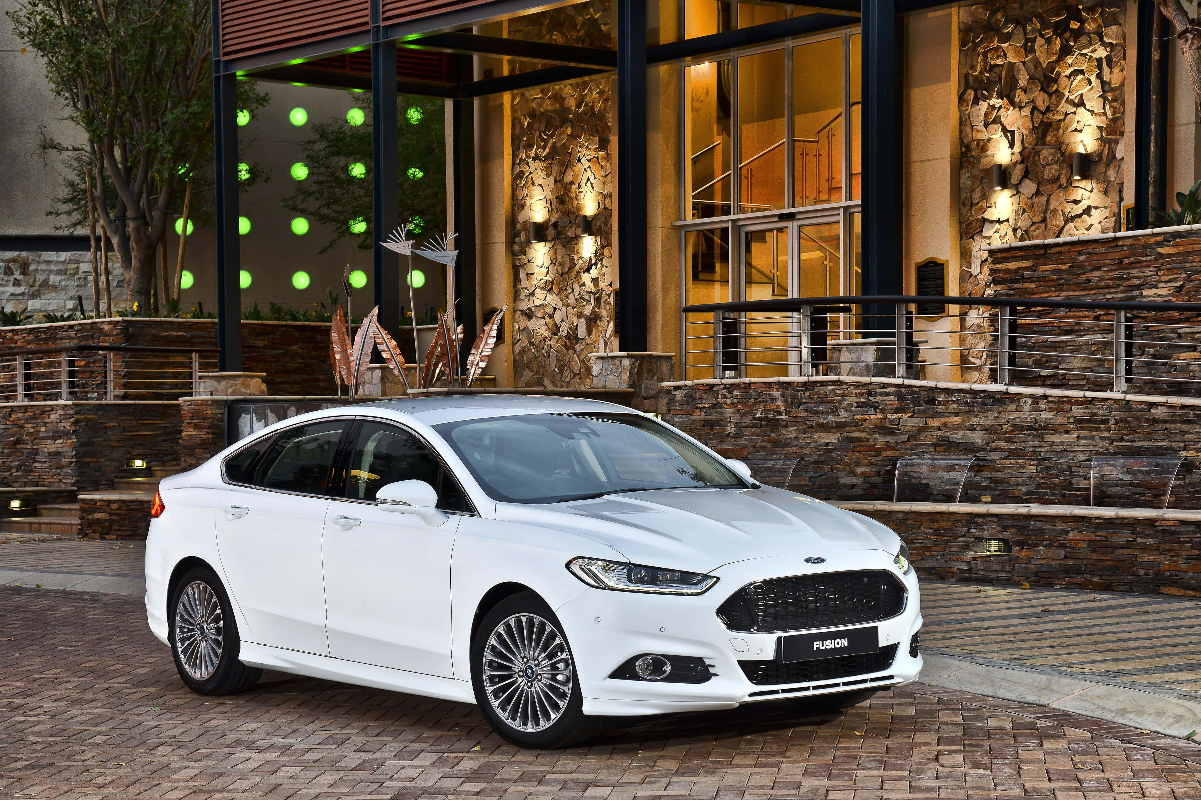 Ford Fusion 桌布 壁紙 — 一輛時尚的白色福特Fusion轎車在夜間停泊在現代石頭和玻璃建築前的磚砌庭院中。