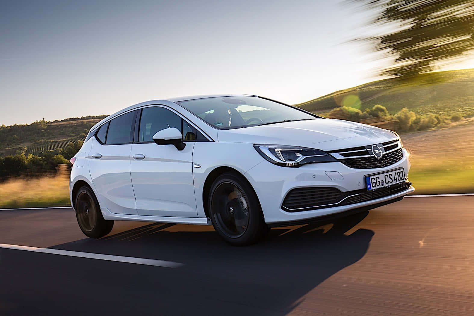 Opel Astra 桌布 壁紙 — 一輛時尚的白色歐寶雅特CS在日落時分沿著蜿蜒的道路疾馳，背景是模糊的金色山丘。
