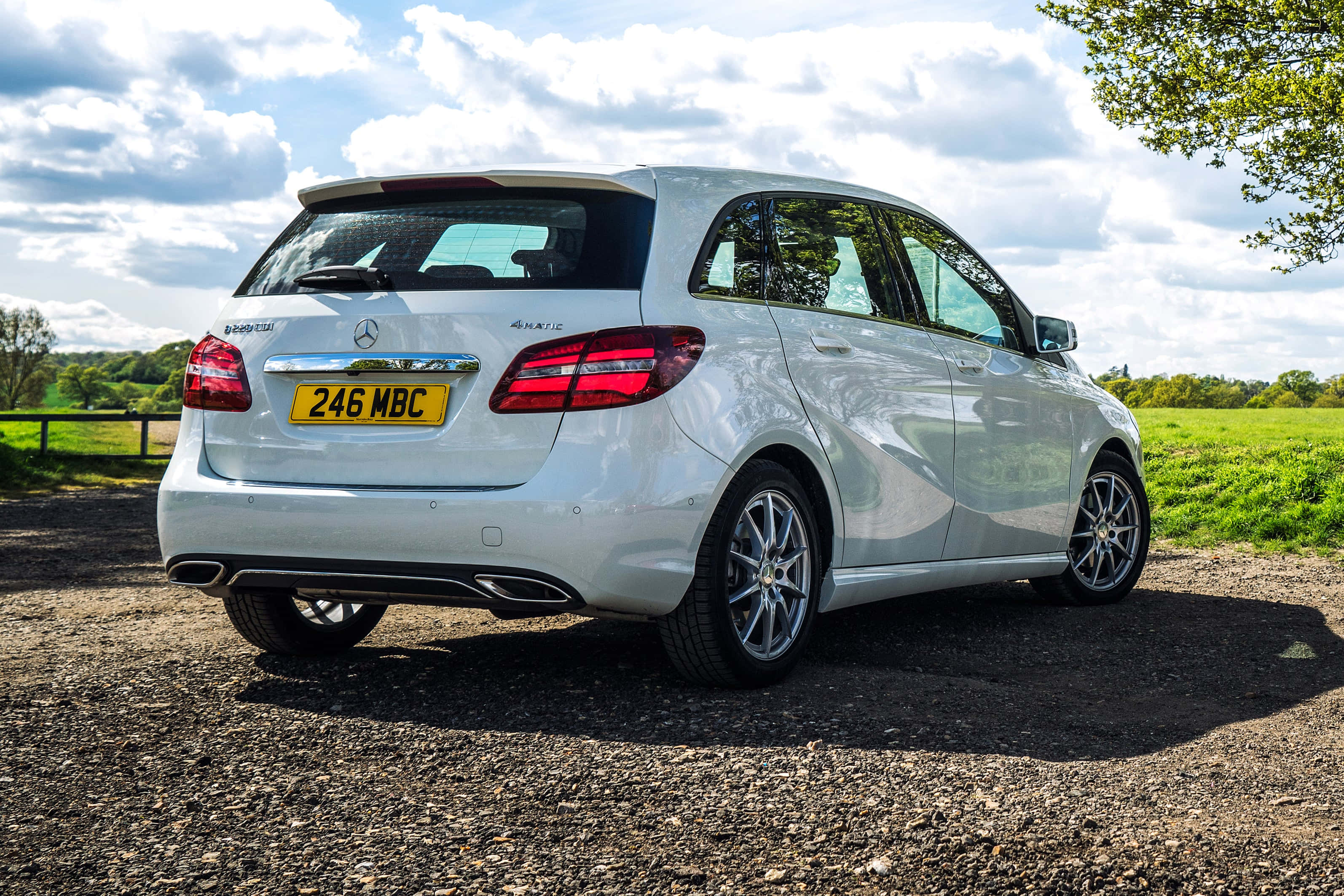 Mercedes Benz B-class 桌布 壁紙 — 一輛時尚的白色平治B-Class停在碎石上，背景有綠色田野和多雲的天空。
