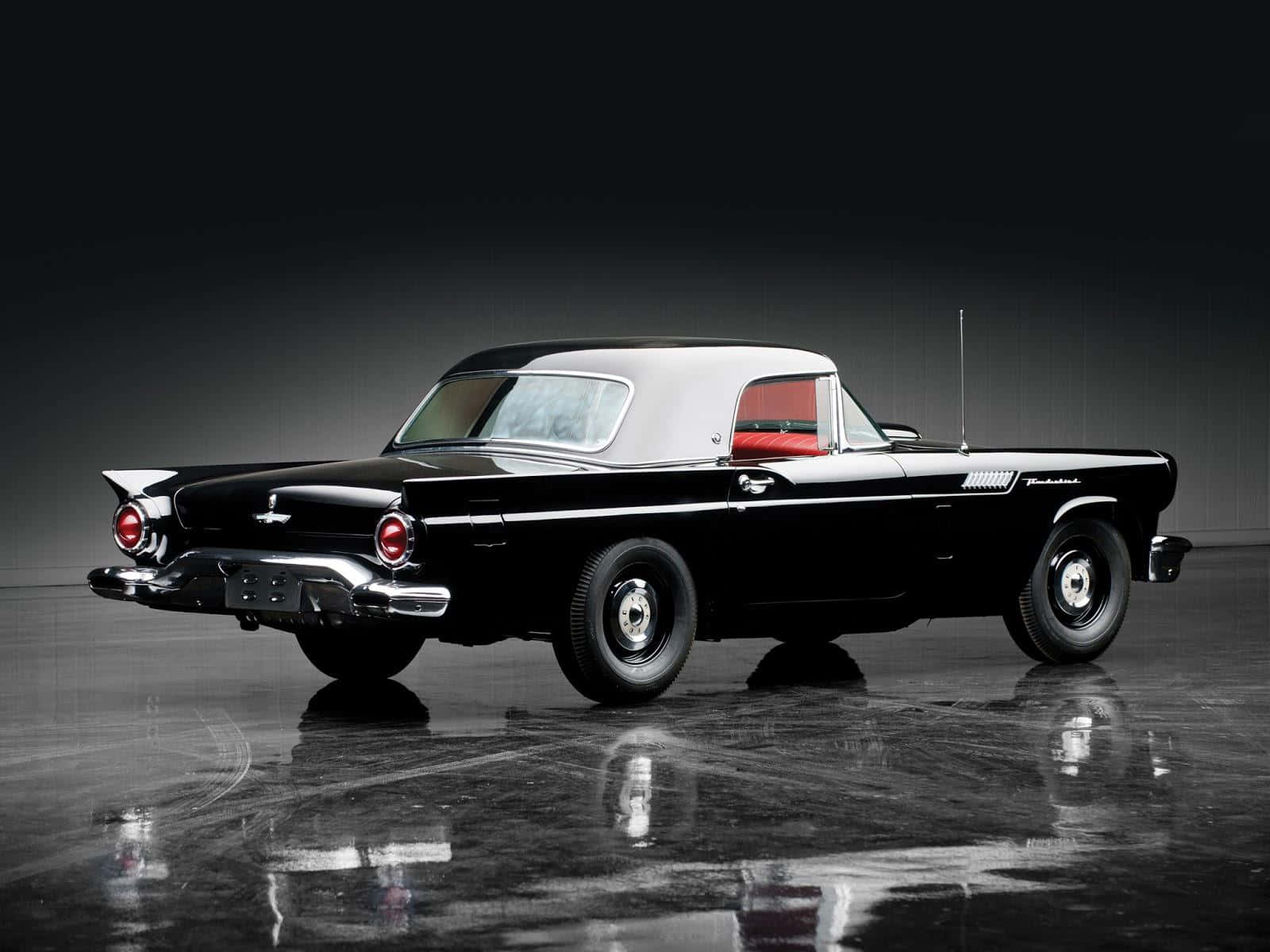 Ford Thunderbird 桌布 壁紙 — 一輛時尚的黑色1950年代福特雷鳥敞篷車，配備白色車頂和紅色內飾，在反射地板上的工作室燈光下閃閃發光。