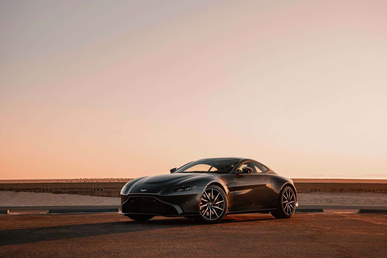 Aston Martin Vantage 桌布 壁紙 — 一輛時尚的黑色Aston Martin跑車停在沙漠公路上，正值黃金時刻，周圍溫暖的光線。