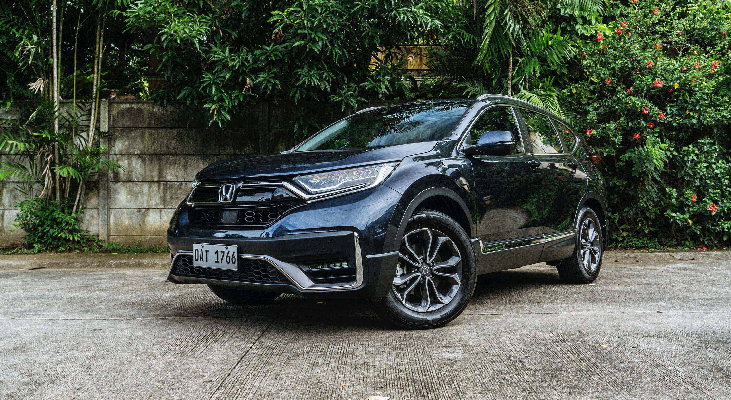 Honda Cr-v 桌布 壁紙 — 一輛時尚的黑色本田CR-V SUV停在混凝土車道上，周圍環繞著茂密的綠色樹葉和盛開的紅色花朵。