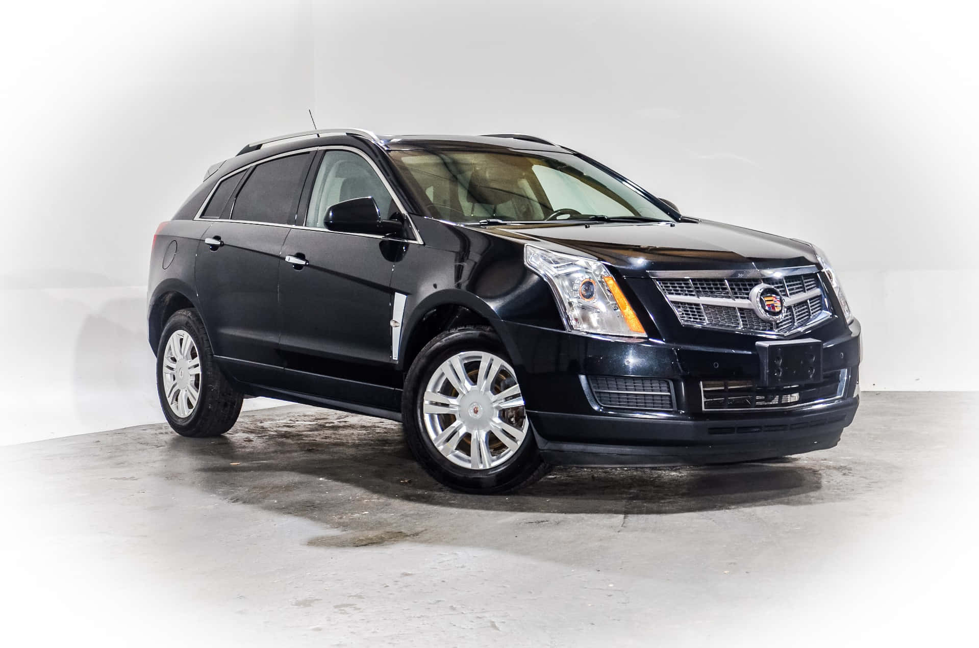 Cadillac Srx 桌布 壁紙 — 一輛時尚的黑色Cadillac SRX SUV在極簡工作室中展示，柔和燈光突顯其拋光鉻合金輪圈和格柵。