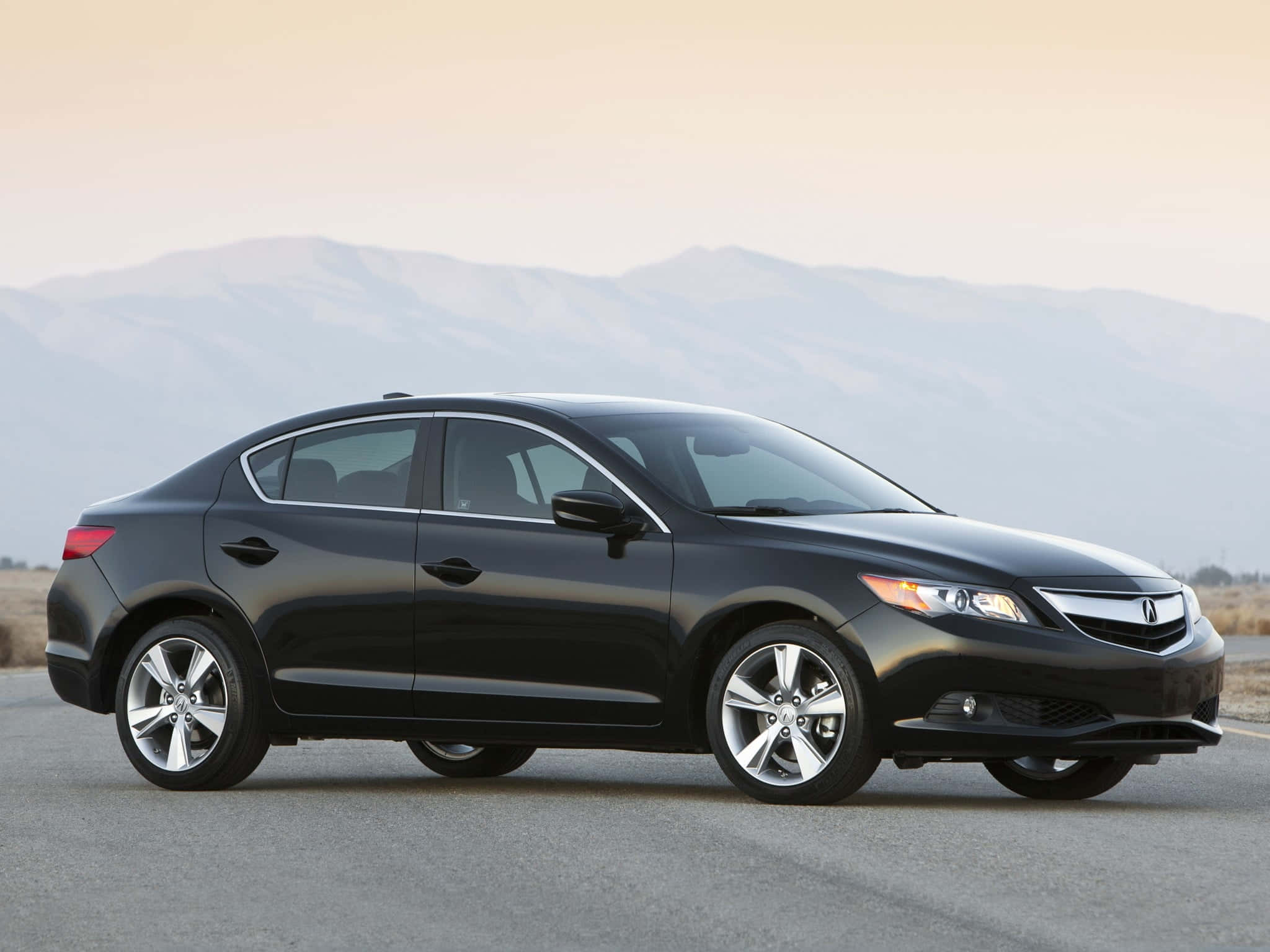 Acura Ilx 桌布 壁紙 — 一輛時尚的黑色轎車停在瀝青路上，遠山在柔和的金色天空下。