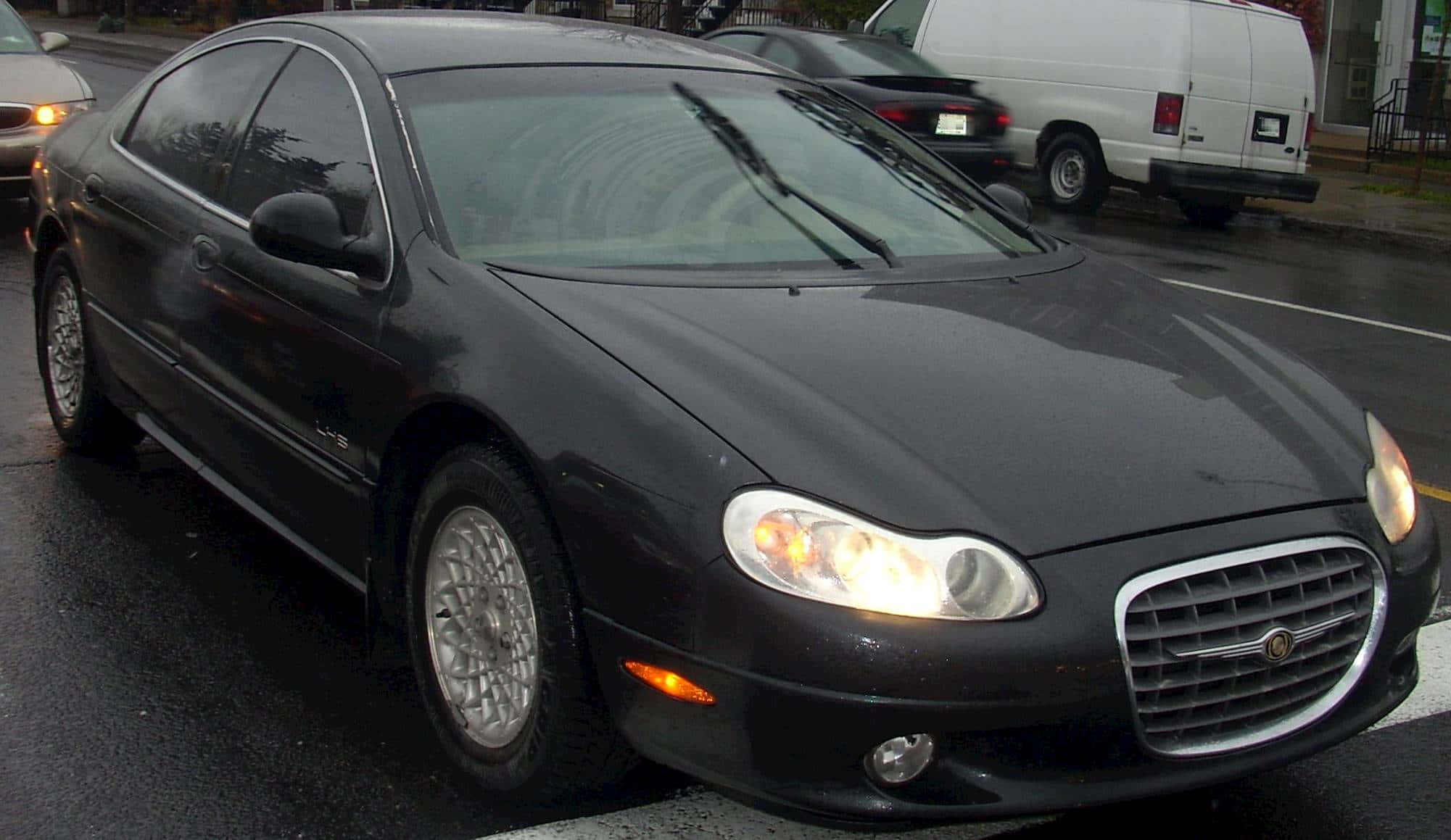 Chrysler Lhs 桌布 壁紙 — 一輛時尚的黑色克萊斯勒LHS轎車停在濕漉漉的城市街道上，車頭燈亮著，擋風玻璃上可見雨滴。