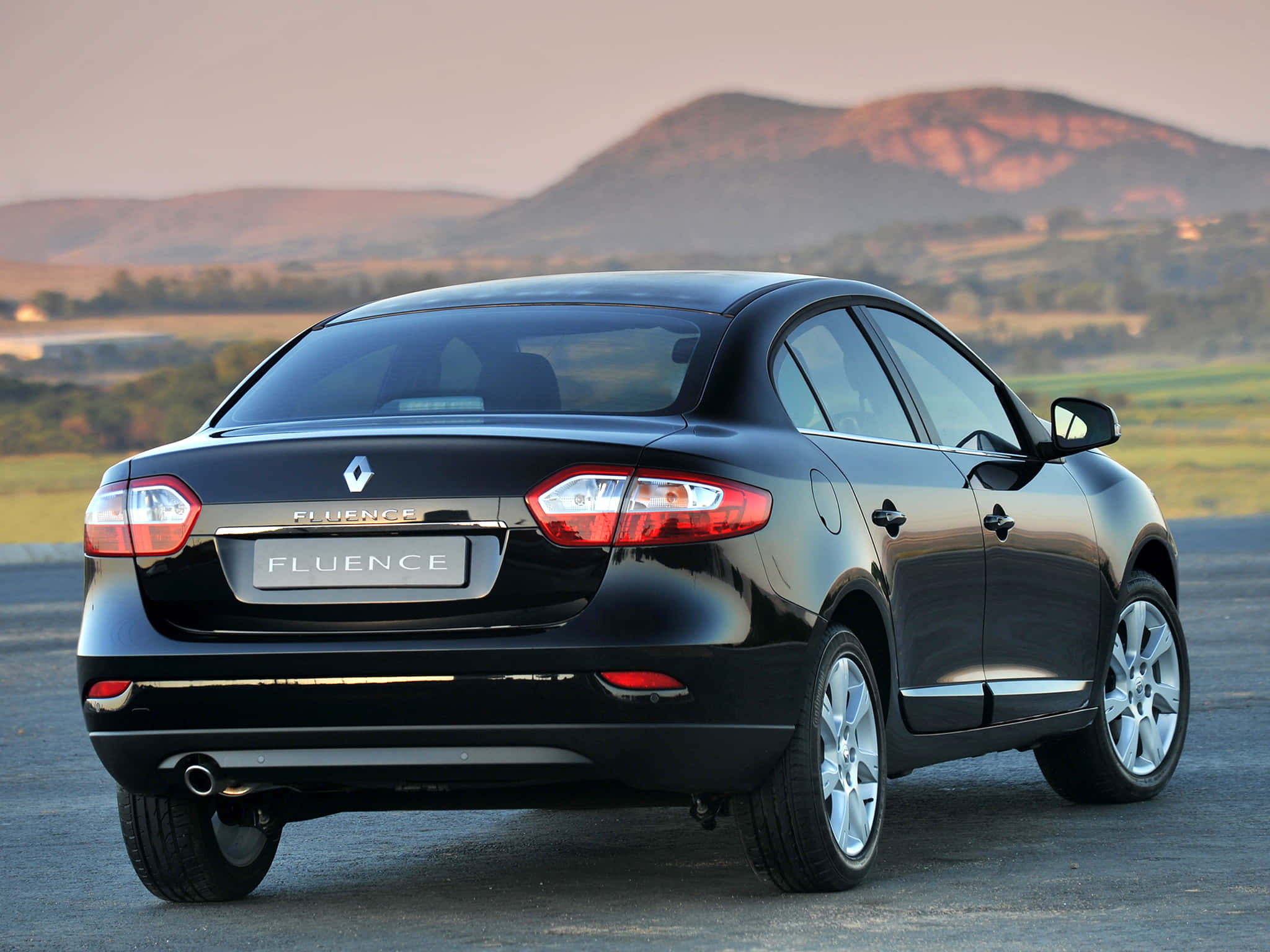 Renault Fluence 桌布 壁紙 — 一輛時尚的黑色雷諾 Fluence 房車停在瀝青路上，背景是起伏的丘陵和柔和的日落光線。