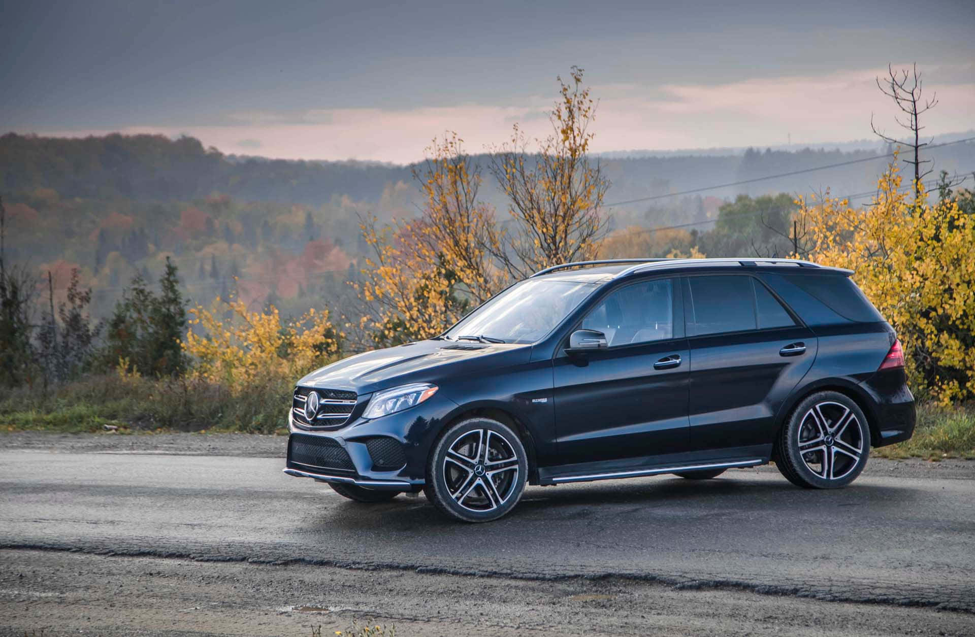 Mercedes Benz Gle-class 桌布 壁紙 — 一輛時尚的黑色梅賽德斯-奔馳SUV停在路邊，周圍有秋樹和起伏的山丘，天空柔和暮色。