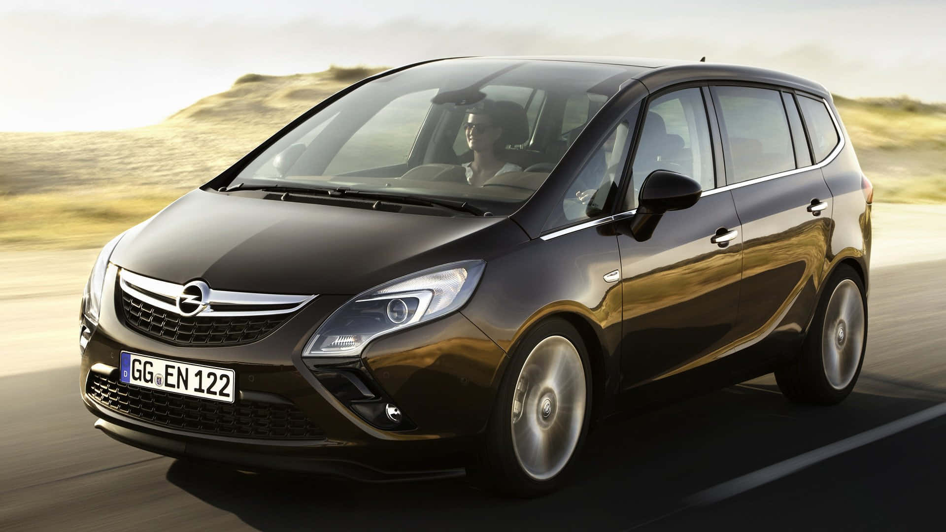 Opel Zafira 桌布 壁紙 — 一輛時尚的黑色Opel Zafira在陽光明媚的道路上快速行駛，背景是模糊的金色山丘。