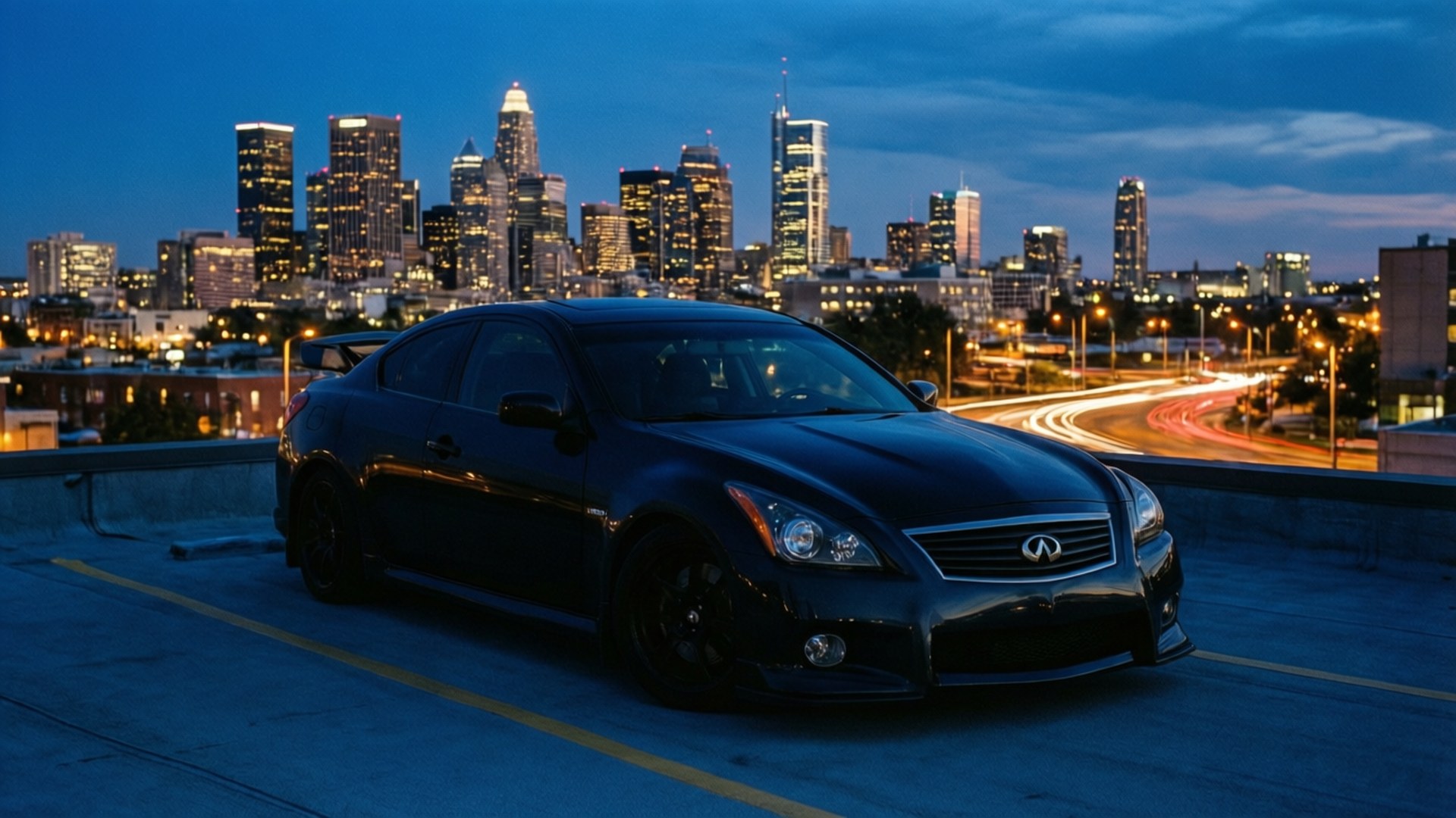 Infiniti G37 桌布 壁紙 — 一輛時尚的黑色跑車在黃昏時停在天台上，背後是發光的城市天際線和光跡。