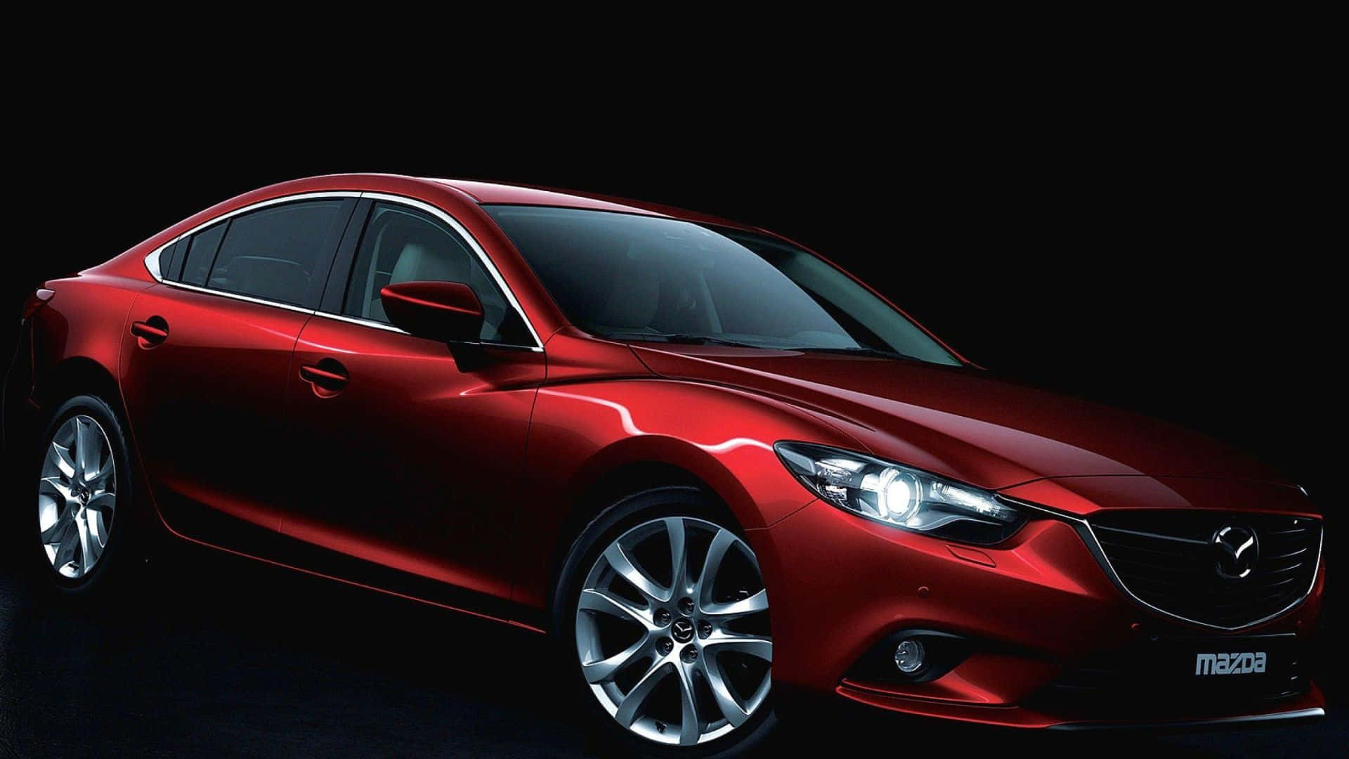 Mazda 6 桌布 壁紙 — 一輛時尚的紅色萬事得轎車在純黑色背景下於攝影棚燈光下閃耀，展示其空氣動力學曲線和拋光合金輪圈。