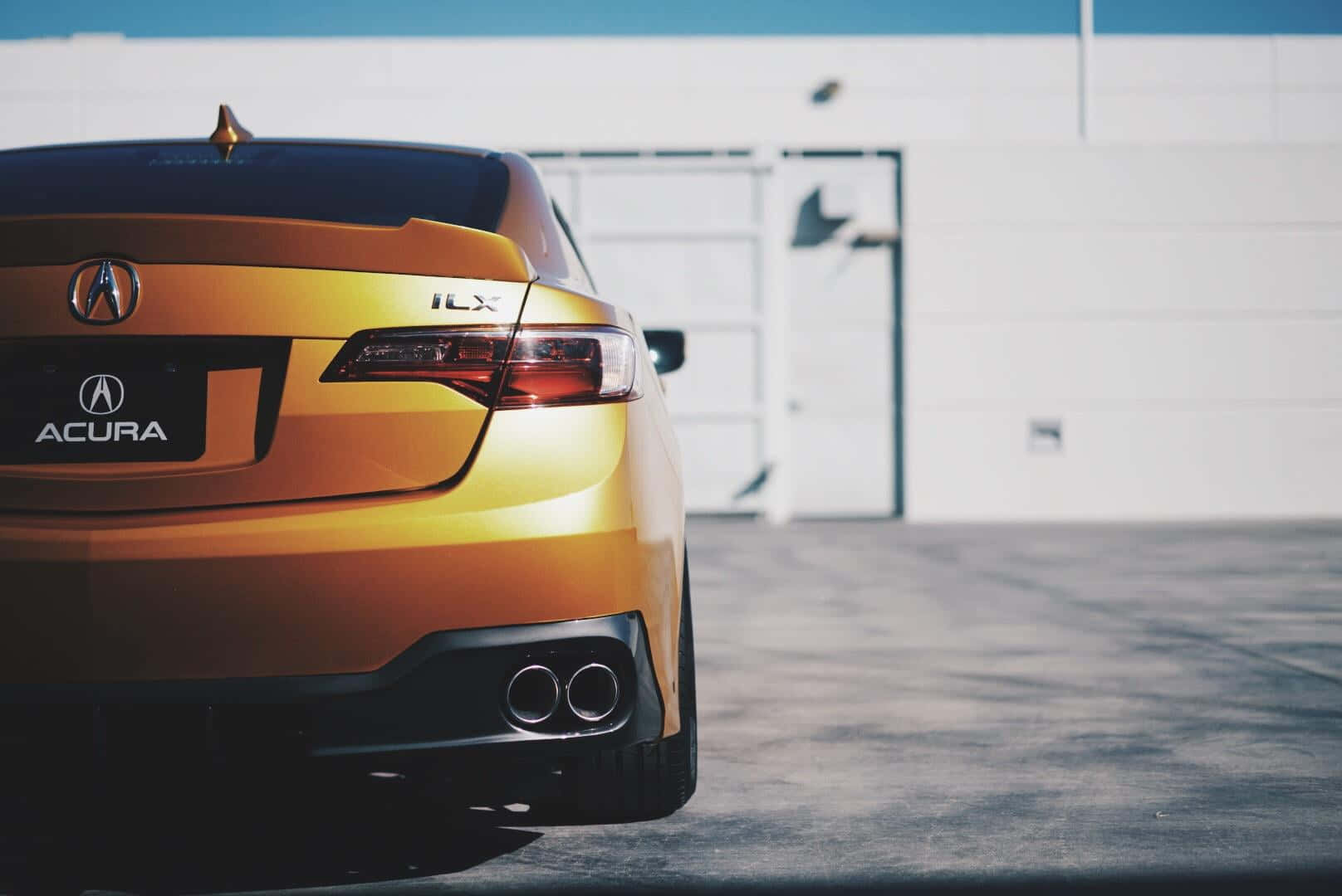 Acura Ilx 桌布 壁紙 — 一輛時尚的黃金Acura ILX跑車在明亮的日光下停在一棟白色工業建築前。