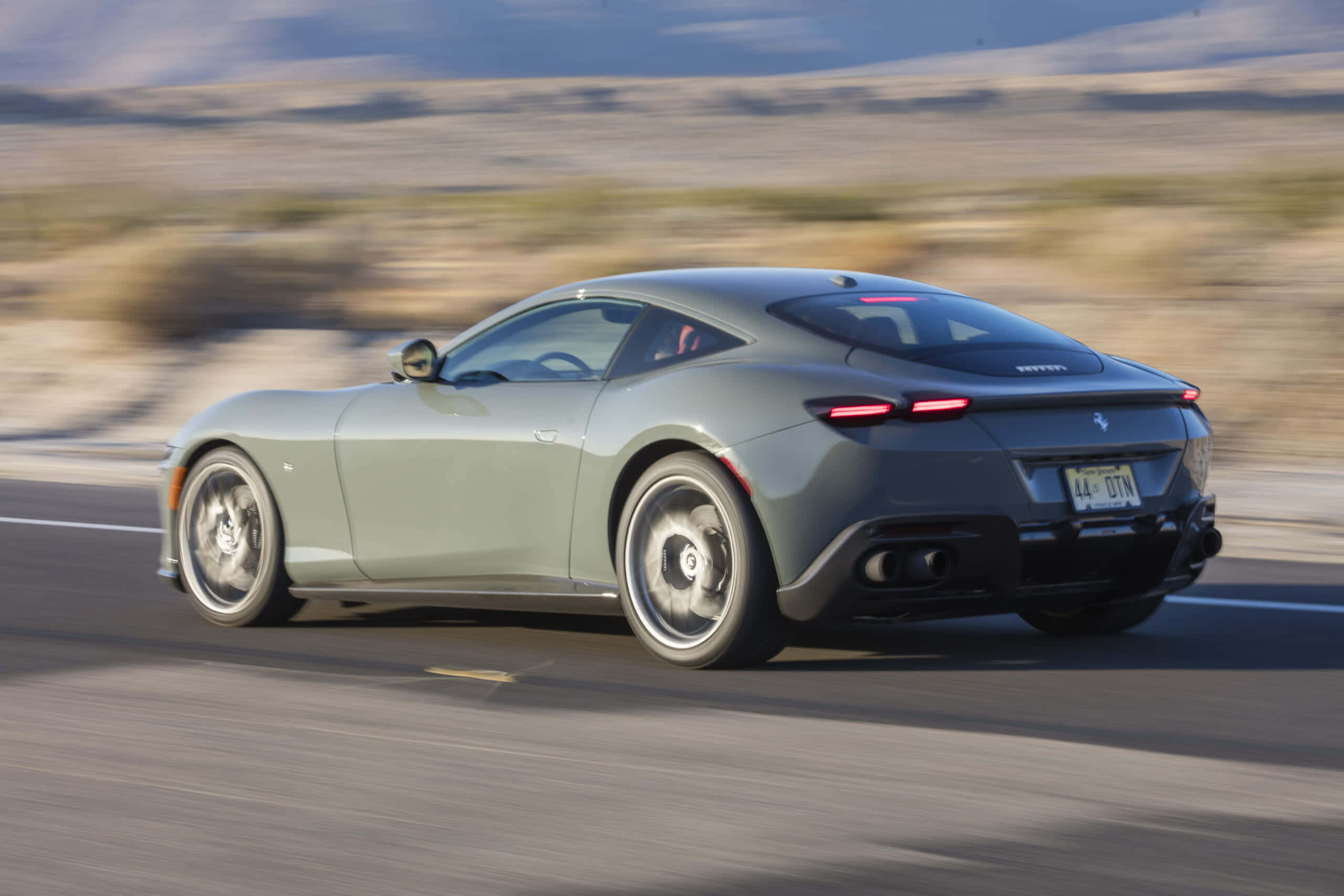 Ferrari Roma 桌布 壁紙 — 一輛時尚的灰色法拉利跑車在沙漠公路上疾馳，周圍環境模糊。