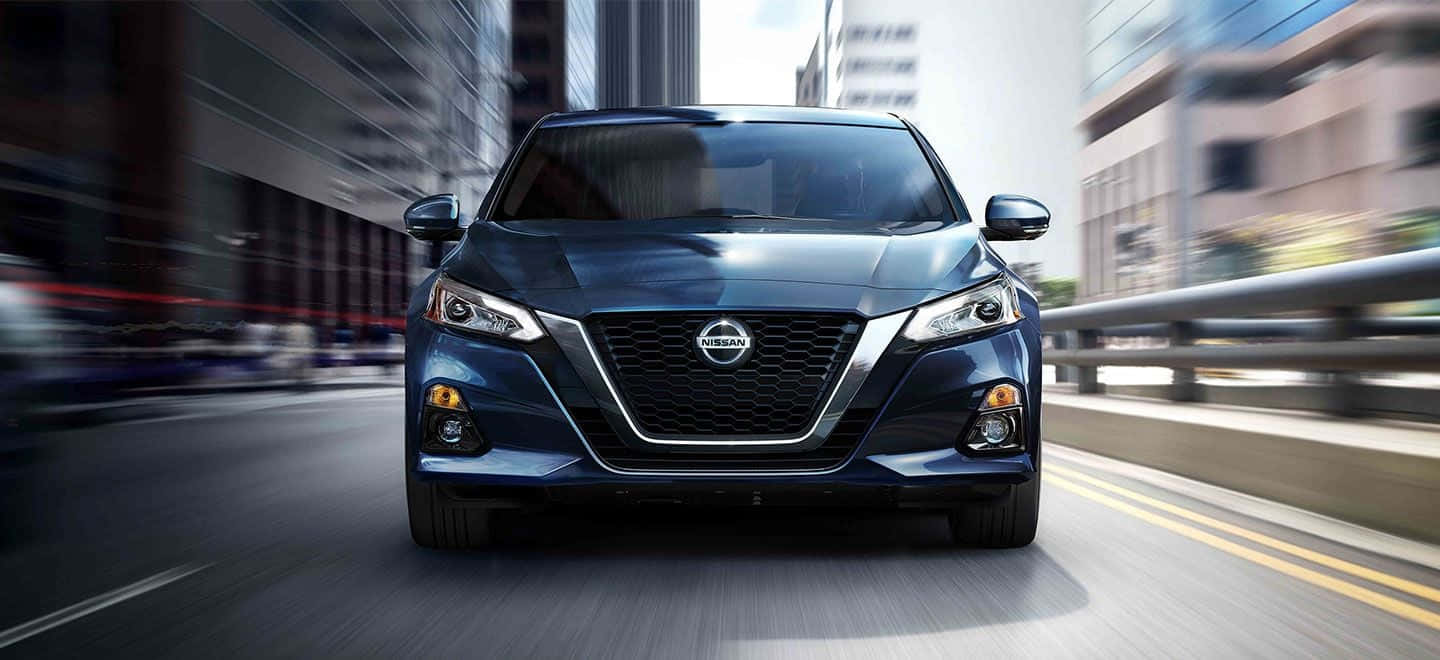 Nissan Altima 桌布 壁紙 — 一輛時尚的藍色日產轎車在城市高速公路上疾馳，模糊的摩天大樓呼嘯而過。