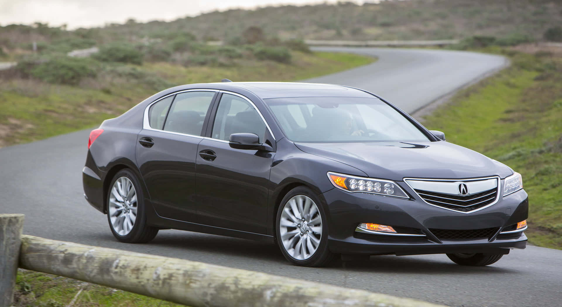 Acura Rlx 桌布 壁紙 — 一輛時尚的深灰色Acura轎車沿著蜿蜒的鄉村道路行駛，兩旁是綠草和木柵欄。