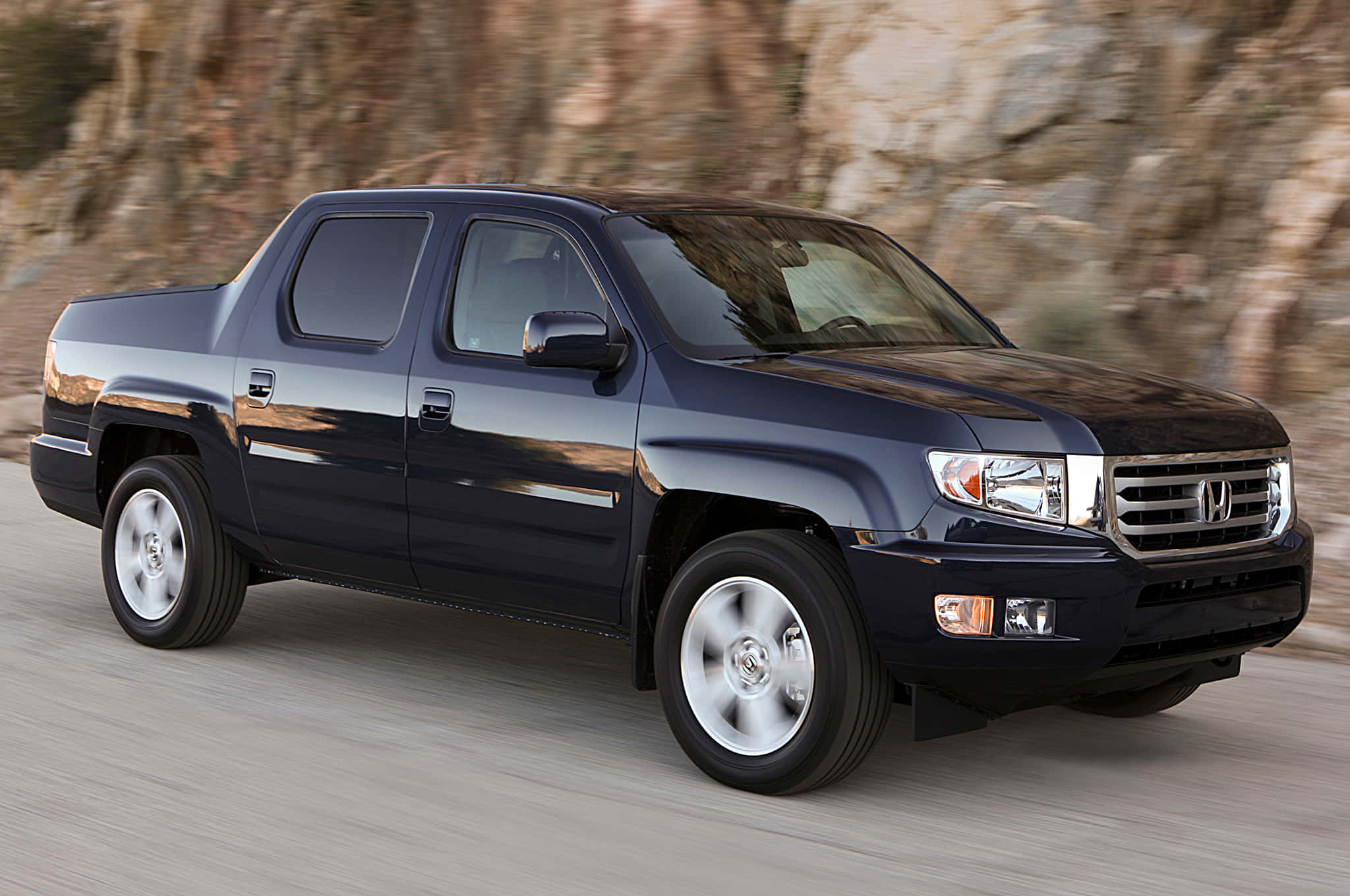 Honda Ridgeline 桌布 壁紙 — 一輛時尚的深藍色本田Ridgeline皮卡車在沙漠公路上飛馳，背景是模糊的岩石峭壁。