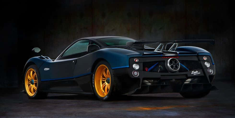 Pagani Zonda Tricolore 桌布 壁紙 — 一輛時尚的深藍色帕加尼Zonda，配以鮮黃色車輪，在燈光昏暗的工業車庫中展示。