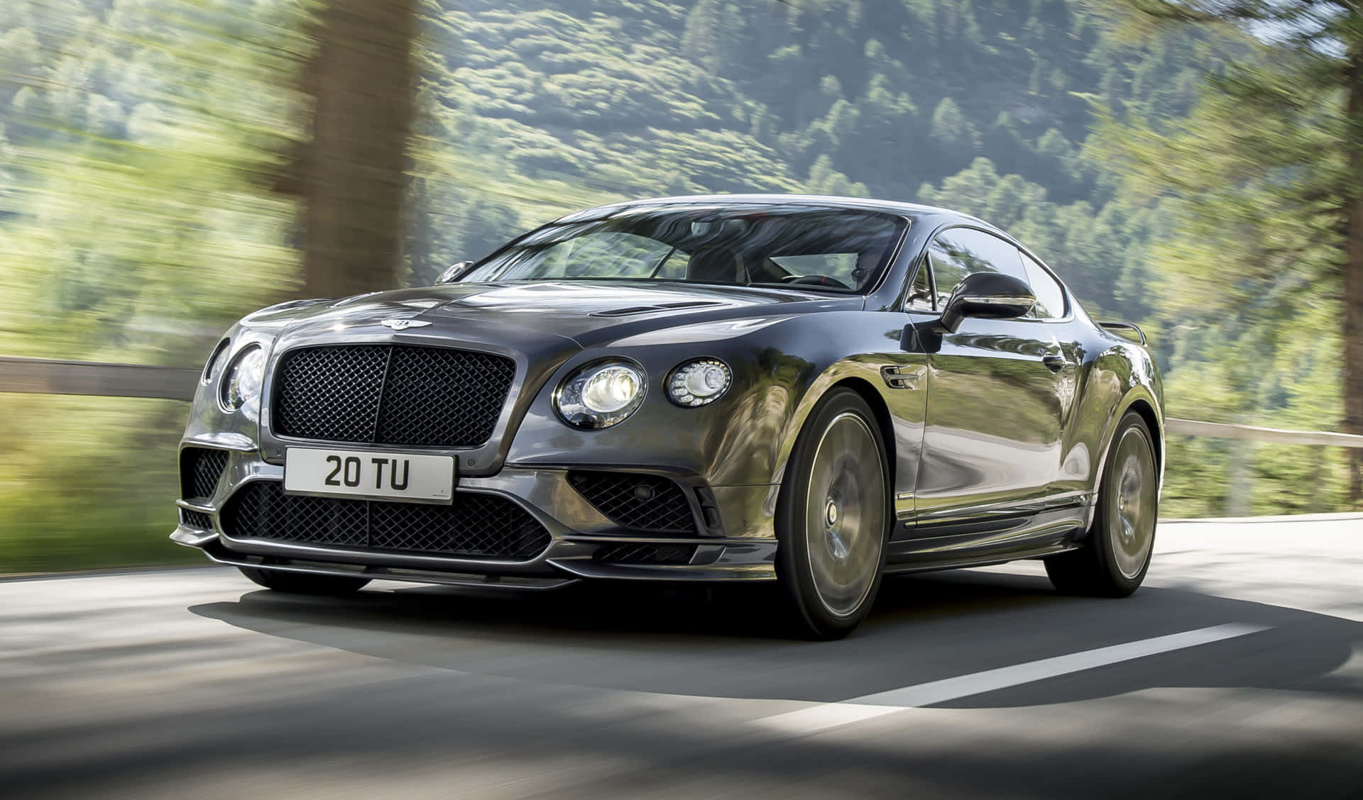 Bentley Continental Supersports 桌布 壁紙 — 一輛時尚的銀色賓利 Continental GT 沿著蜿蜒的山路疾馳，茂密的綠色森林在身後模糊掠過。