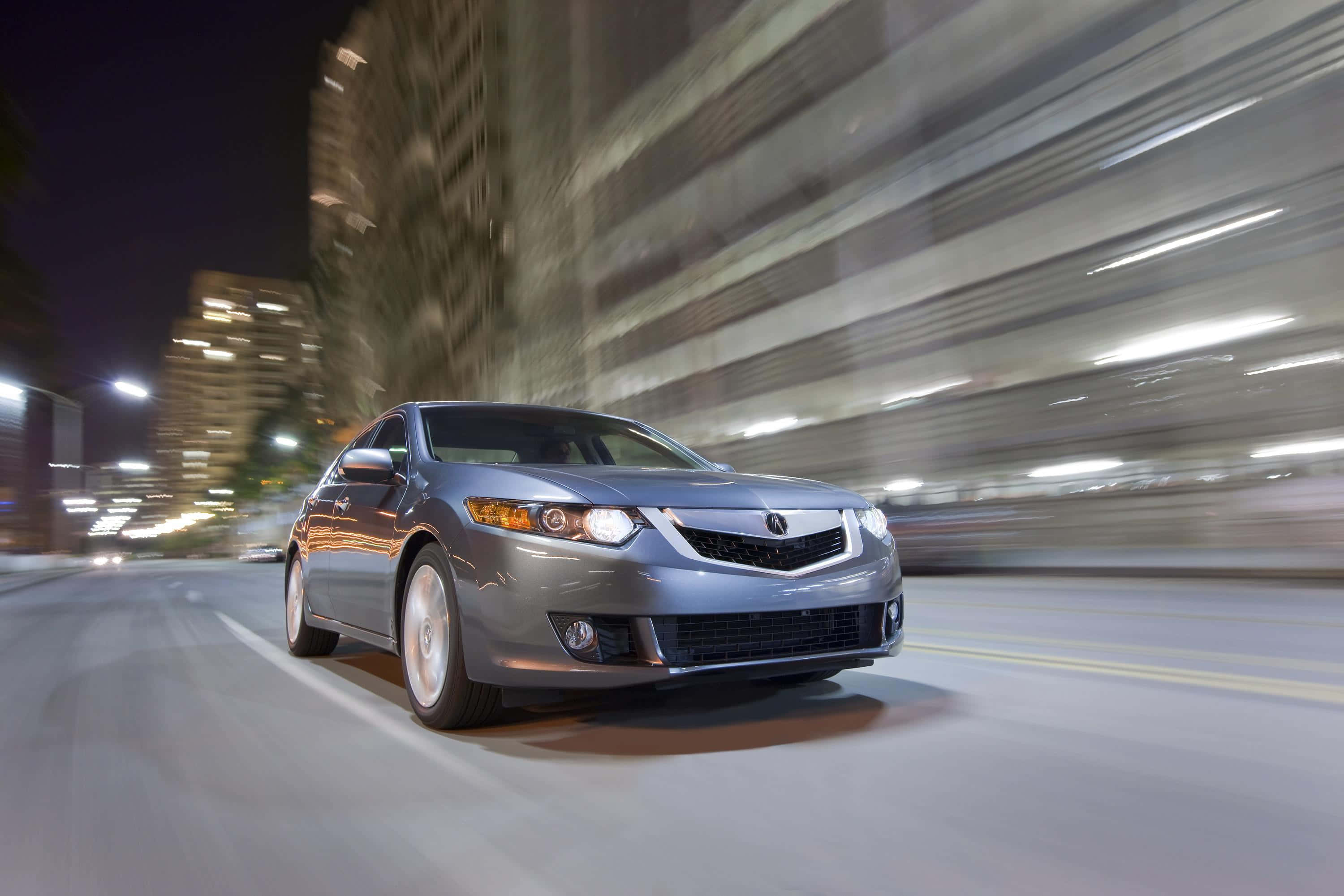 Acura Tsx 桌布 壁紙 — 一輛時尚的銀色轎車在燈火通明、高樓林立的模糊夜景中疾馳。