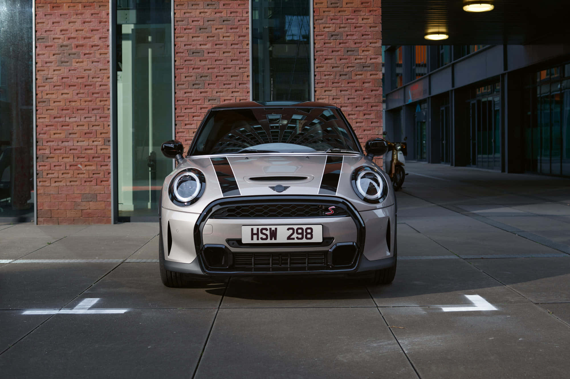 Mini Cooper S 桌布 壁紙 — 一輛銀色MINI Cooper S帶有黑色賽車條紋，停在磚砌建築前，在人工燈光下。