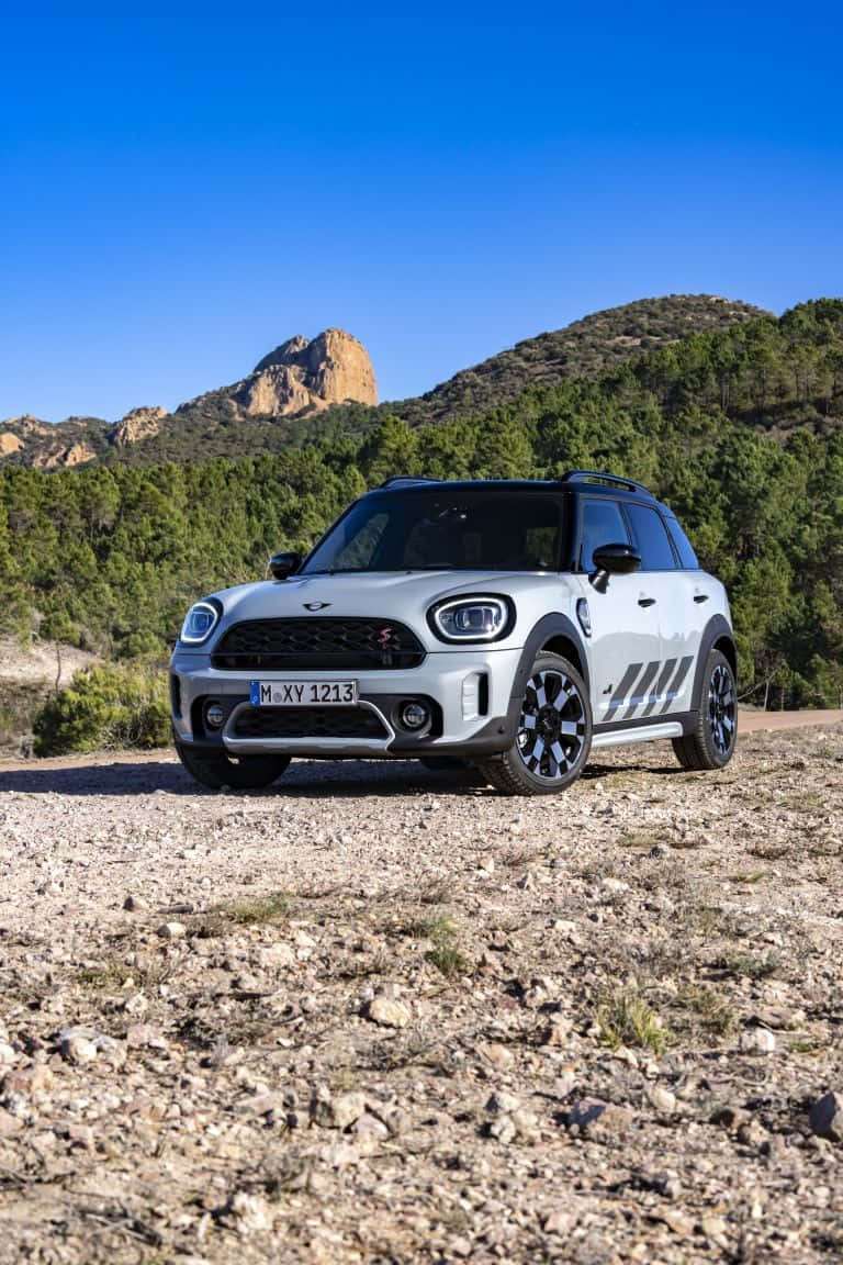  壁紙 — 一輛銀色MINI Countryman SUV停泊在岩石泥土小徑上，周圍有綠色山丘和岩石山峰，天空清澈湛藍。