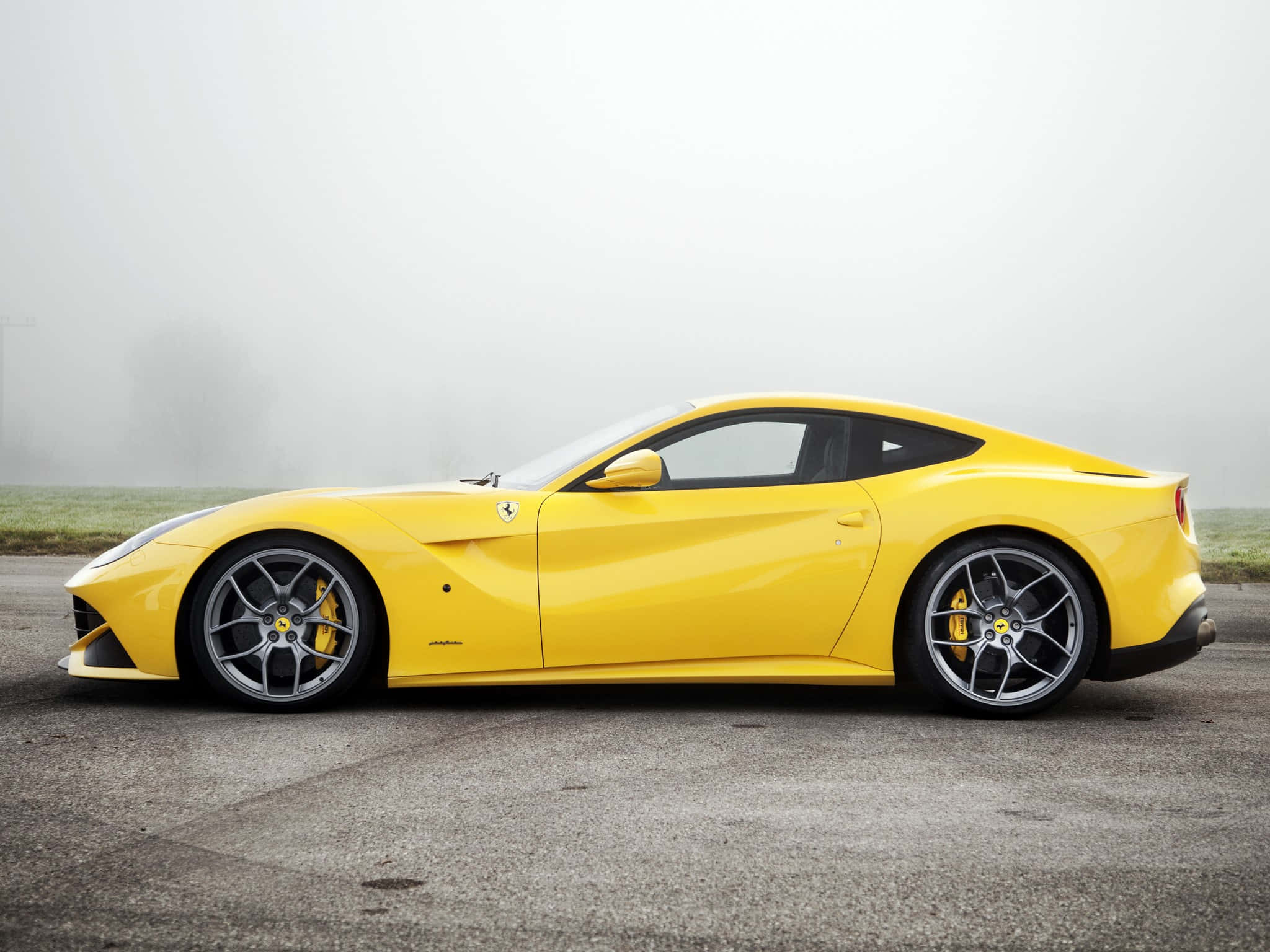 Ferrari F12 Berlinetta 桌布 壁紙 — 一輛充滿活力的黃色法拉利跑車在灰色瀝青路上的霧氣晨光中閃耀。