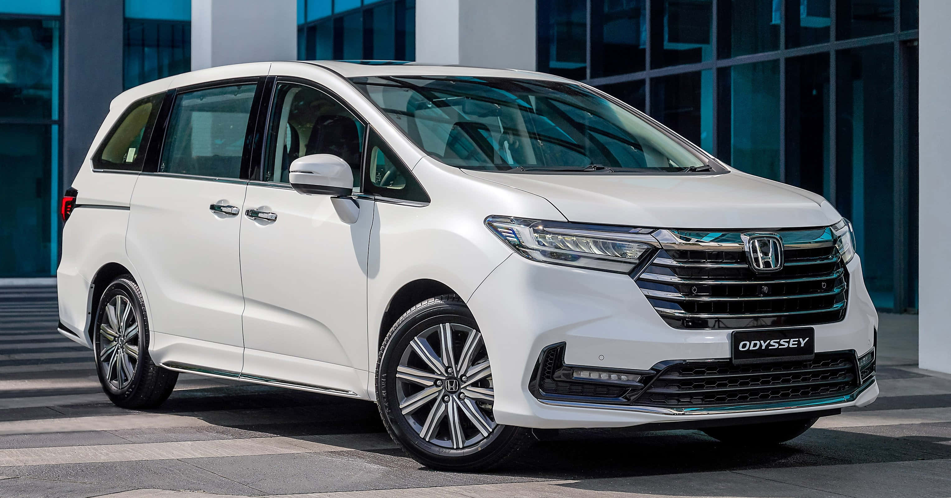 Honda Odyssey 桌布 壁紙 — 一輛純白色的本田Odyssey小型貨車停在一棟現代玻璃建築前，在明亮的日光下。