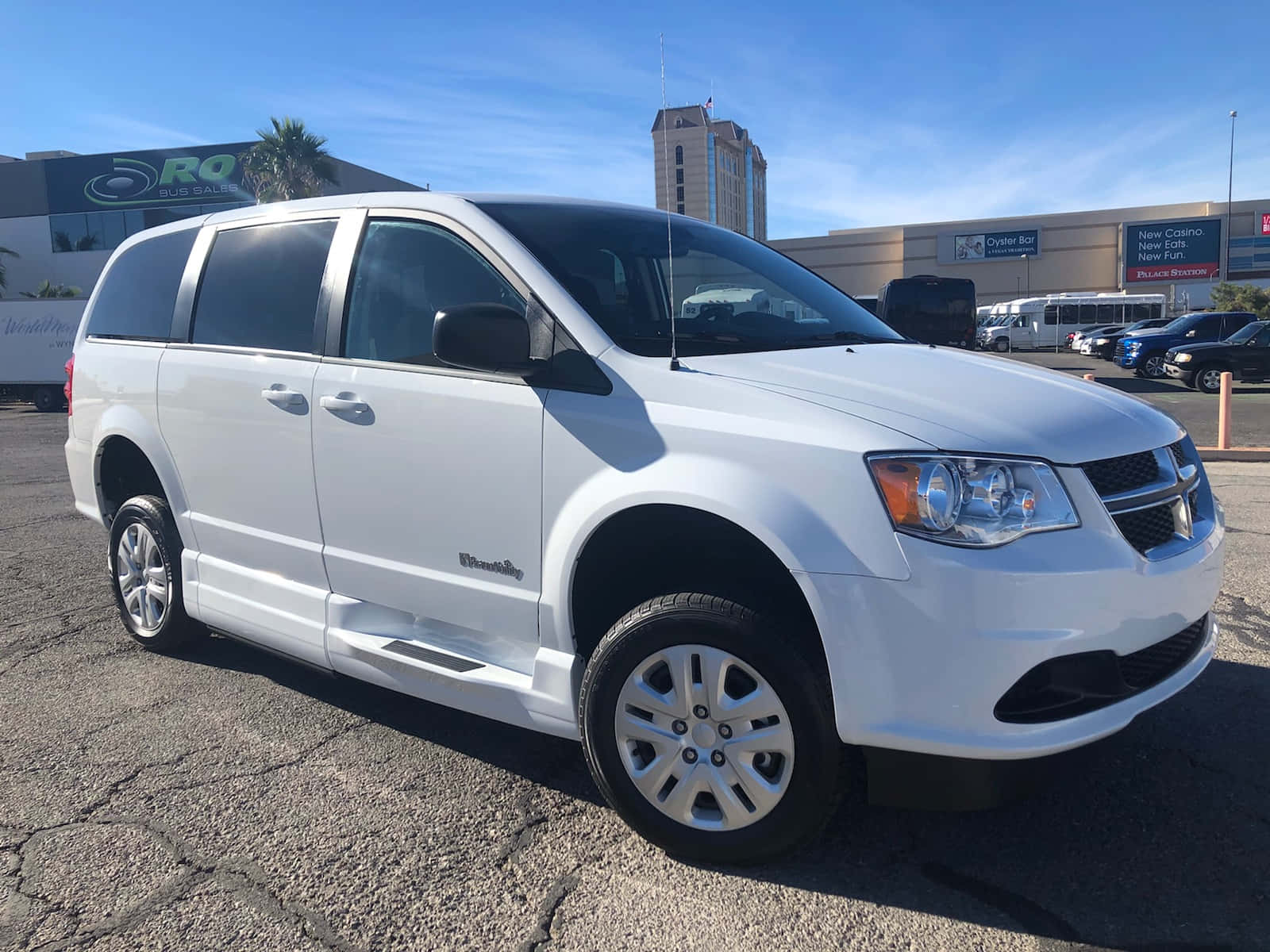 Chrysler Voyager 桌布 壁紙 — 一輛純白色的道奇Grand Caravan小型貨車停在裂開的瀝青路上，背景是晴朗的藍天和一座賭場建築。