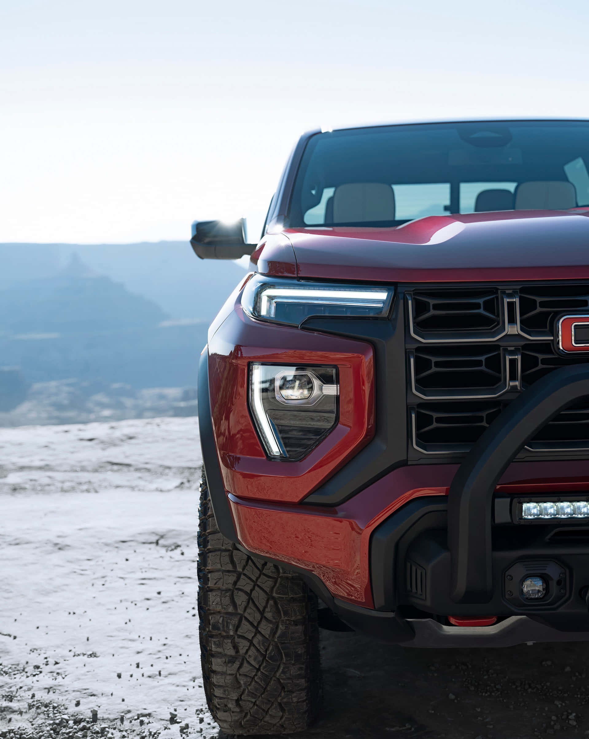 Gmc Canyon 桌布 壁紙 — 一輛大膽的紅色越野卡車，配備堅固輪胎和LED燈，在晴朗的天空下停泊在白雪覆蓋的山頂觀景點。