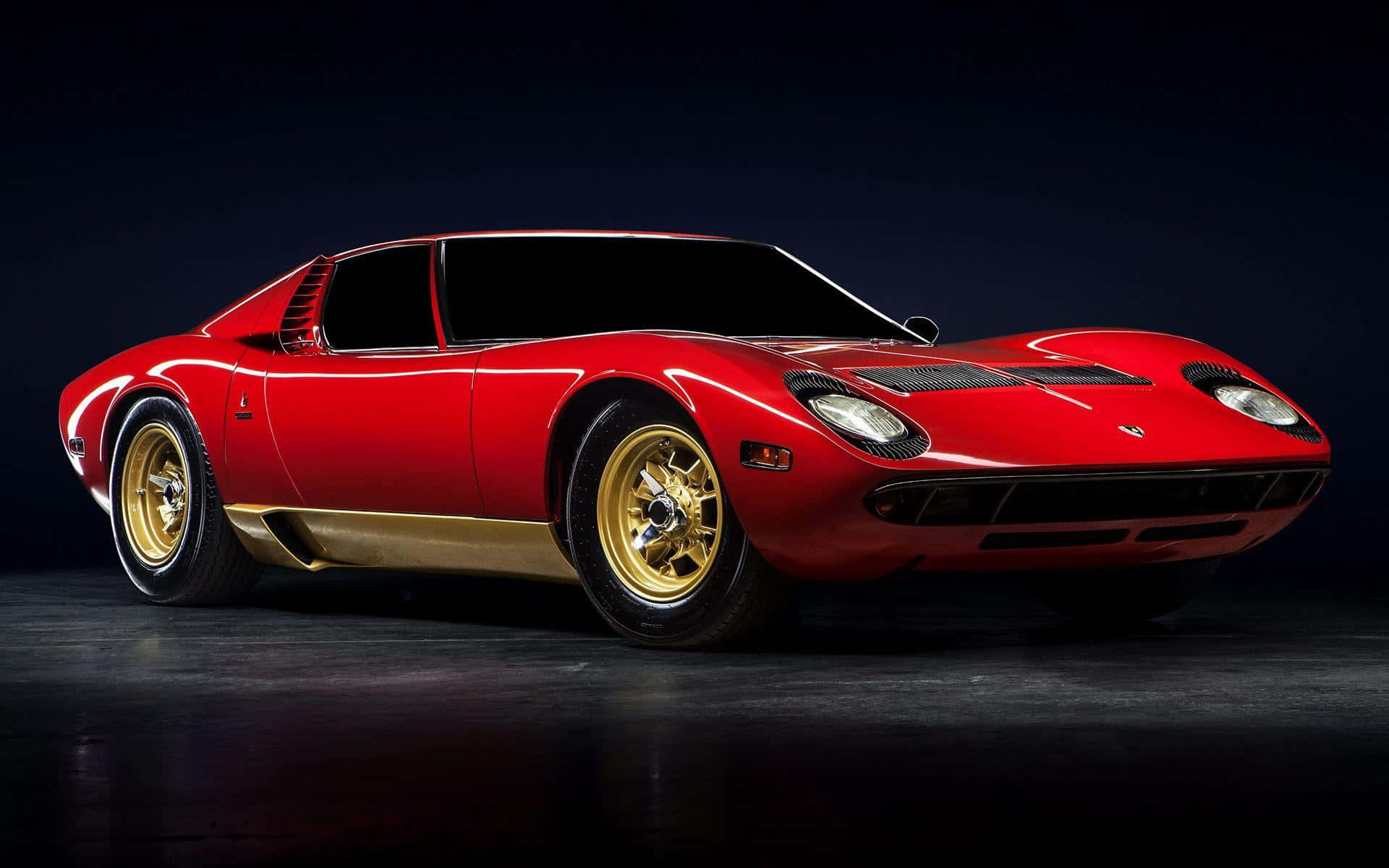Lamborghini Miura 桌布 壁紙 — 一輛帶有金色飾邊和輪轂的亮紅色林寶堅尼 Miura 在深色背景下的攝影棚燈光中閃耀。