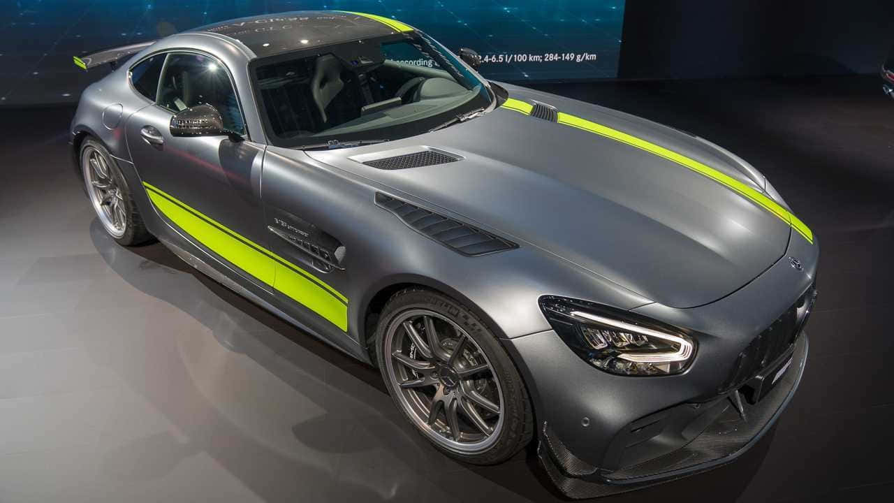  壁紙 — 一輛光滑的啞光灰色 Mercedes-AMG GT R 跑車，帶有螢光綠色賽車條紋，在明亮的展廳燈光下展示。