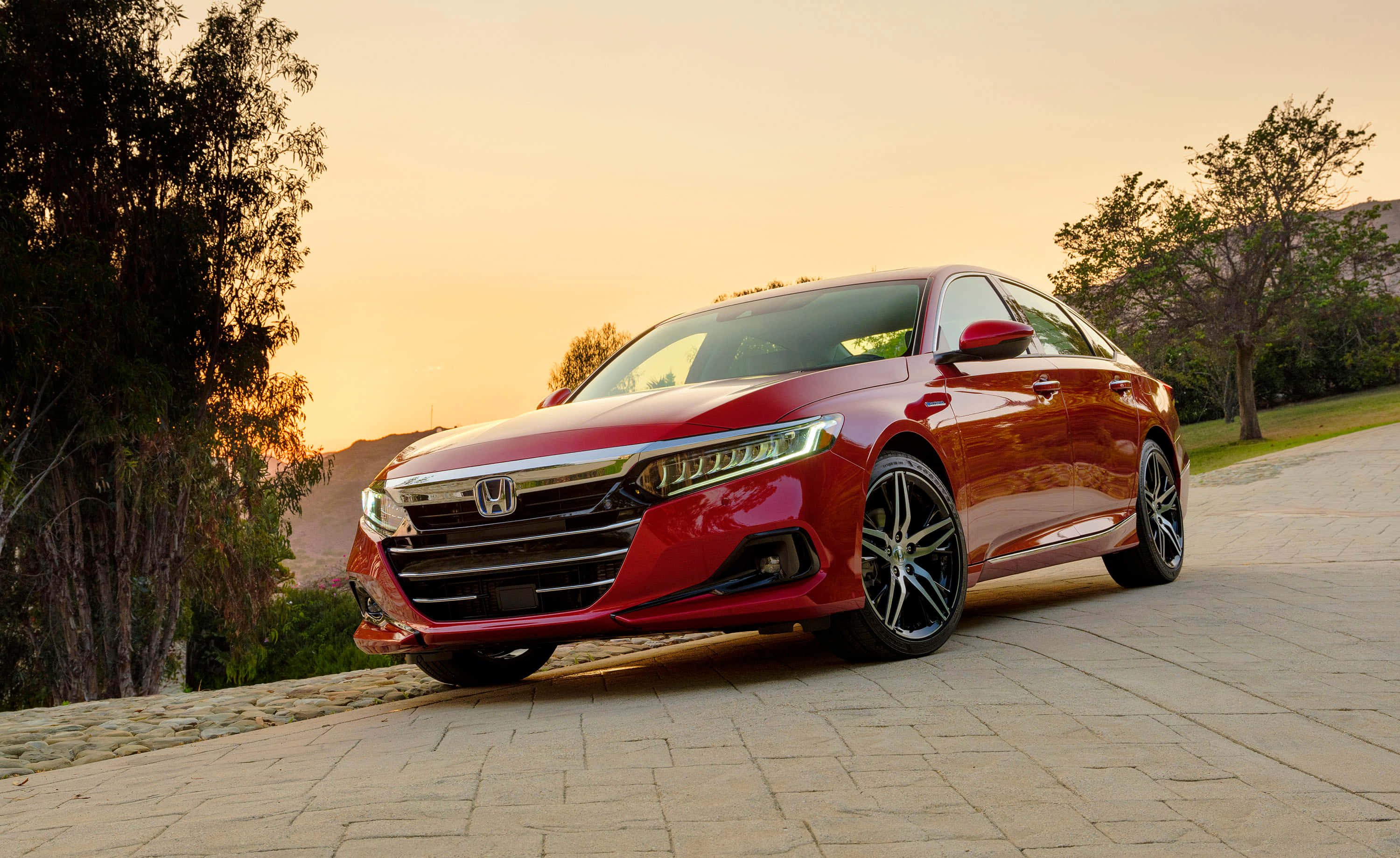 Honda Accord 桌布 壁紙 — 一輛光亮的紅色本田雅閣在黃金時段停泊在石頭車道上，背景有樹木和山丘。