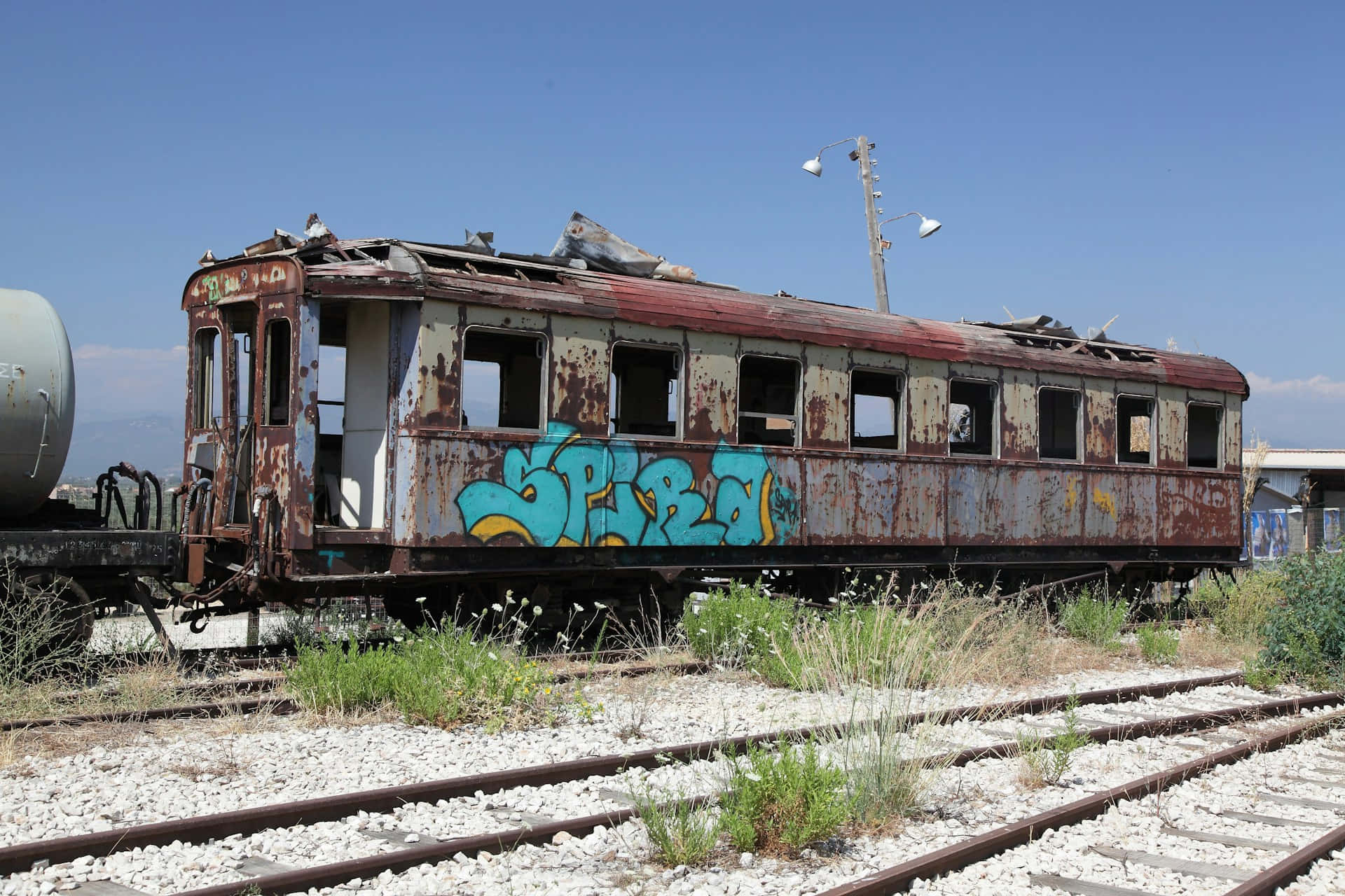  壁紙 — 一輛生鏽廢棄的火車車廂帶有藍色塗鴉，停在長滿雜草的路軌上，天空清澈湛藍。