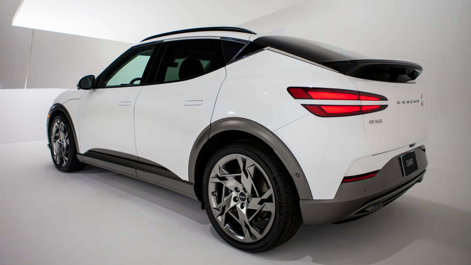 Genesis Gv60 桌布 壁紙 — 一輛時尚的白色 Genesis GV60 電動 SUV 在簡約的工作室中展示，線條簡潔，紅色尾燈閃爍。